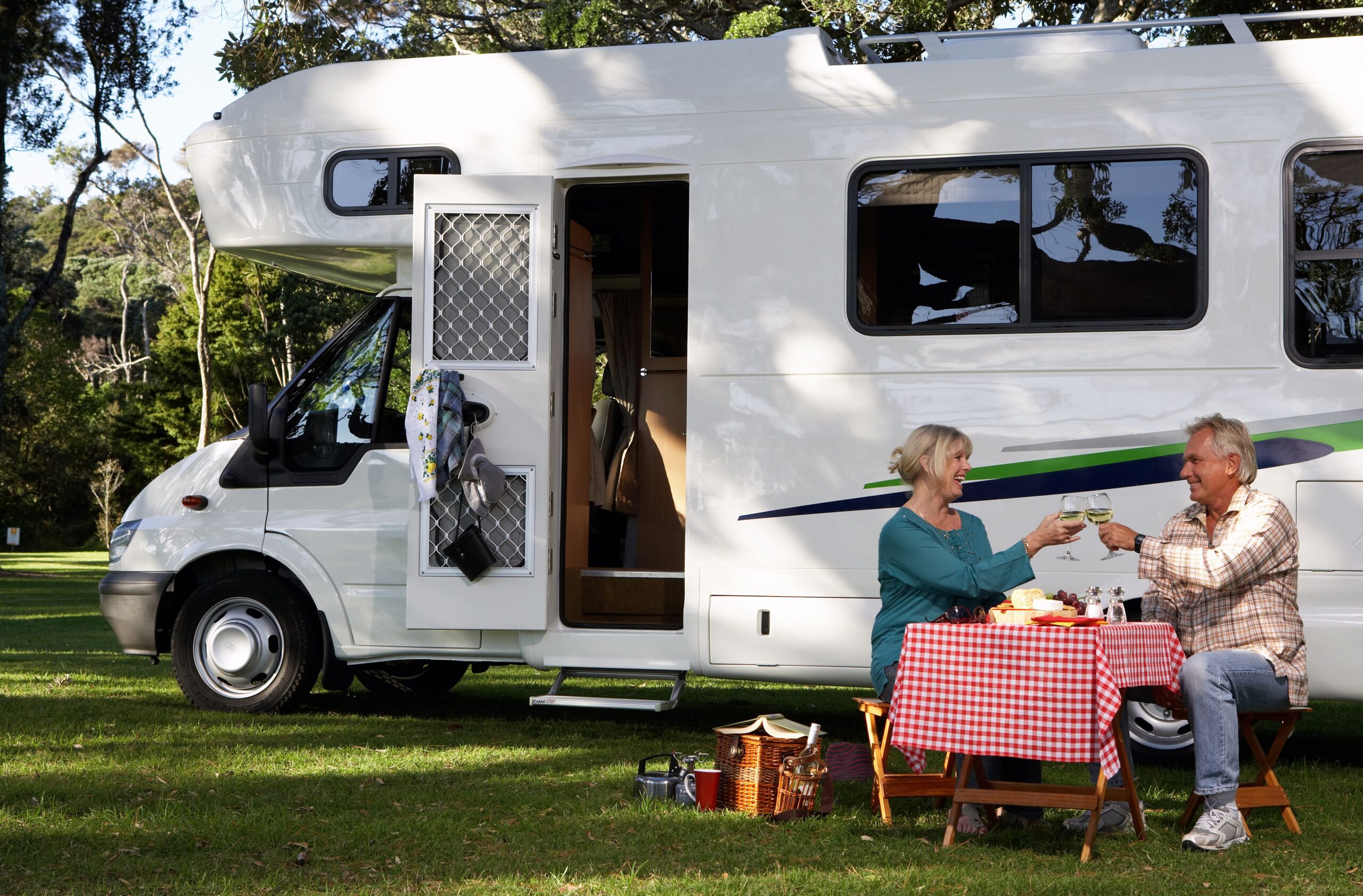 couple sharing wine on picnic table outside rv in grass below trees