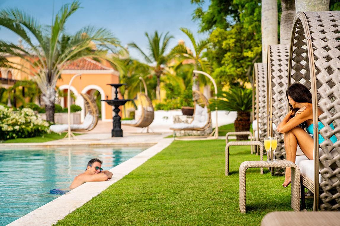 man relaxing in pool, woman seated, mimosas on table