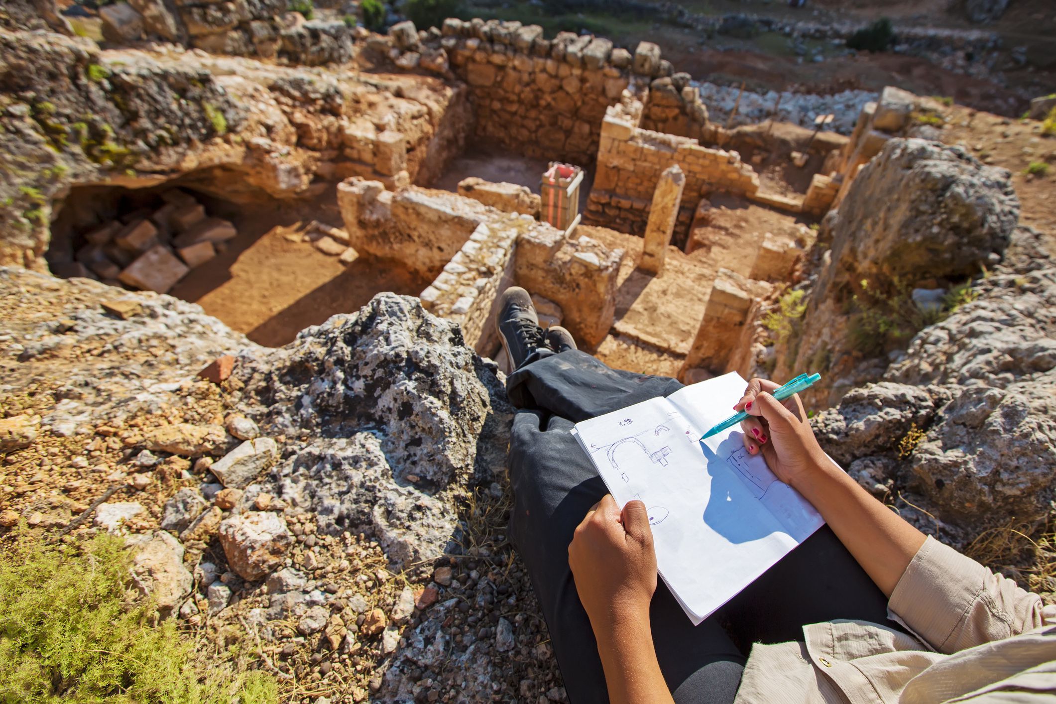 archaeologist sitting overlooking ruins drawing sketch of site plan