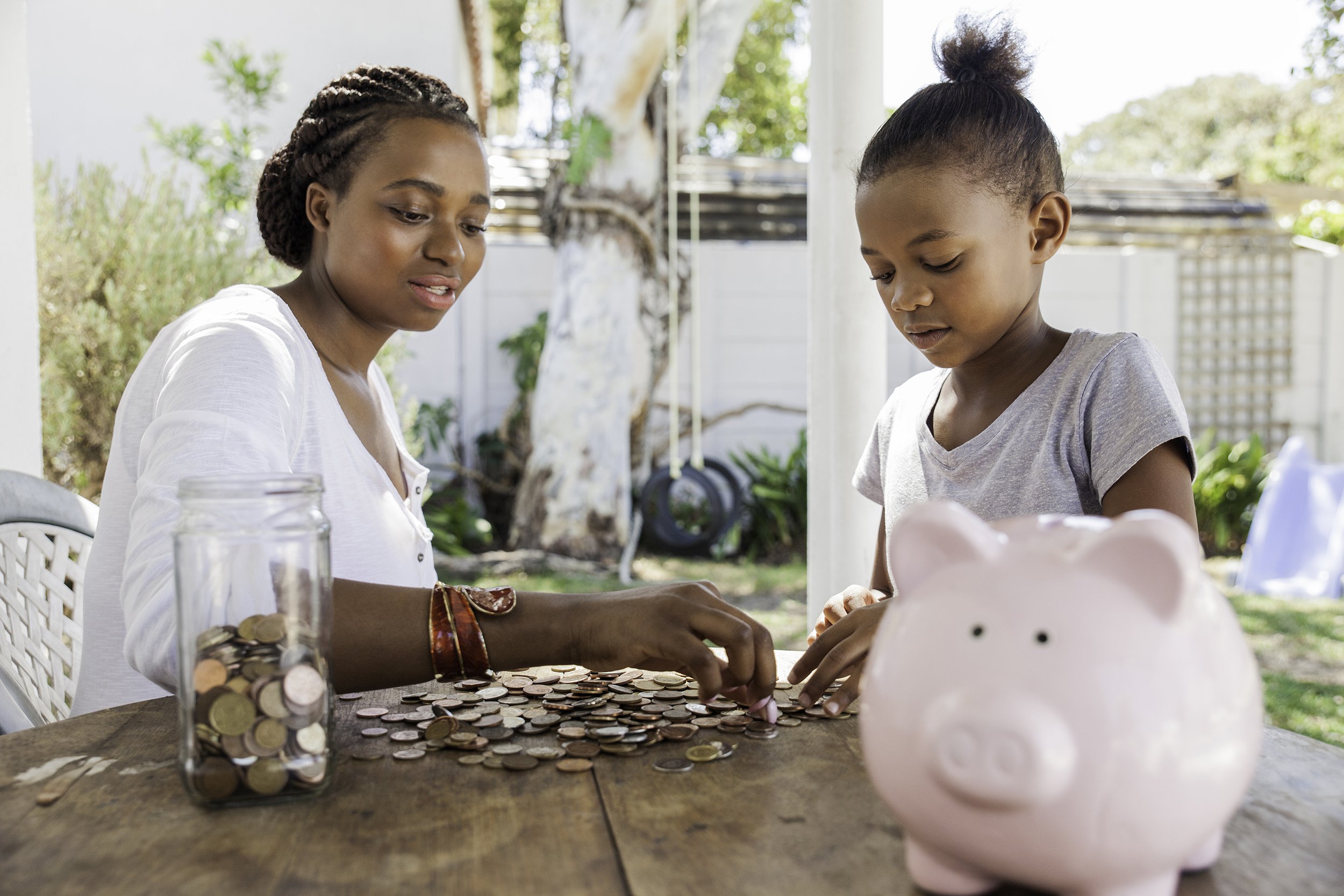 mom counting coins with her daughter on table outside