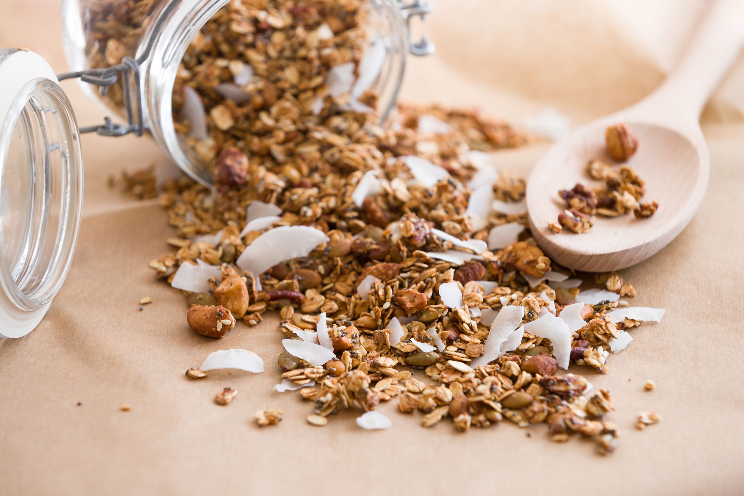 glass jar of homemade organic granola with coconut and pecans on the baking paper background