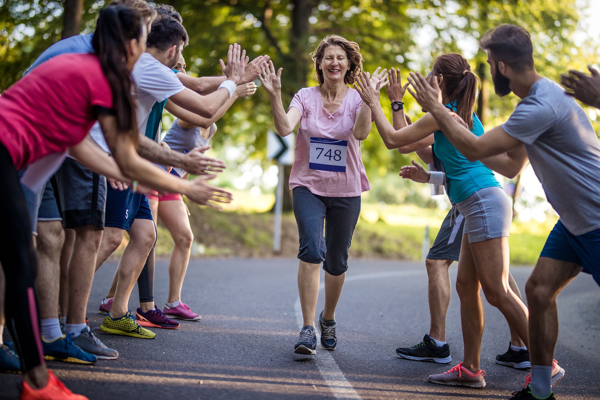 senior woman finishing marathon race and greeting with group of supporters
