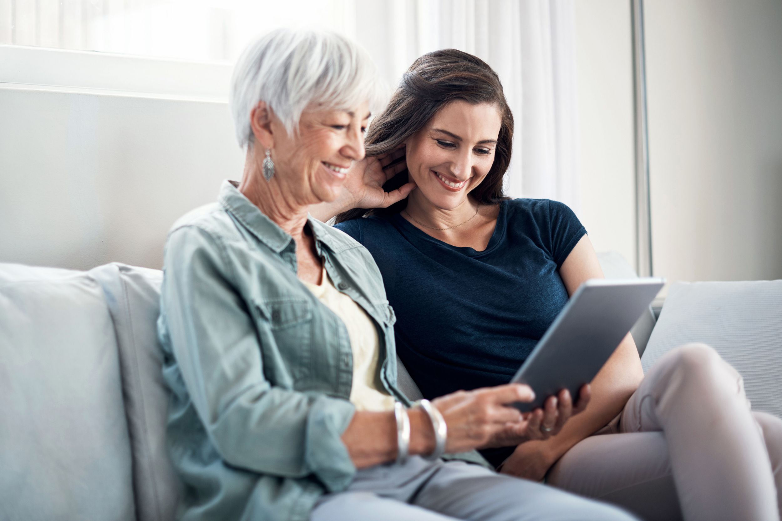 mother and adult daughter looking at tablet together while on couch at home