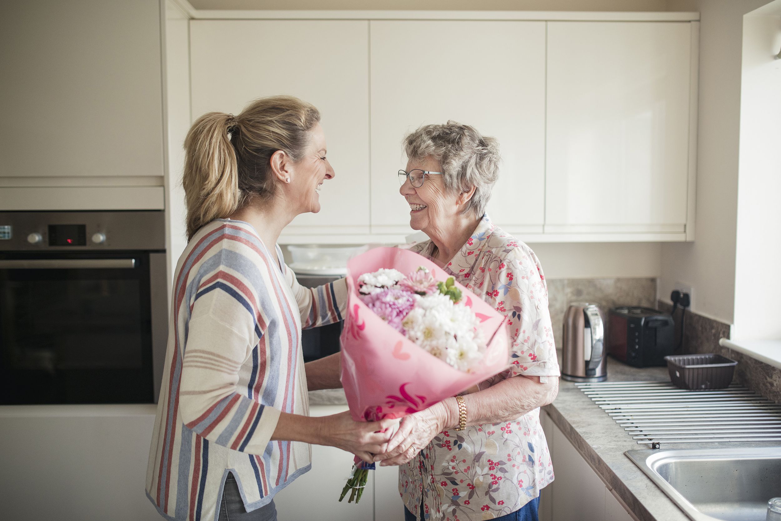 adult daughter giving mother flowers and seeing her in the kitchen