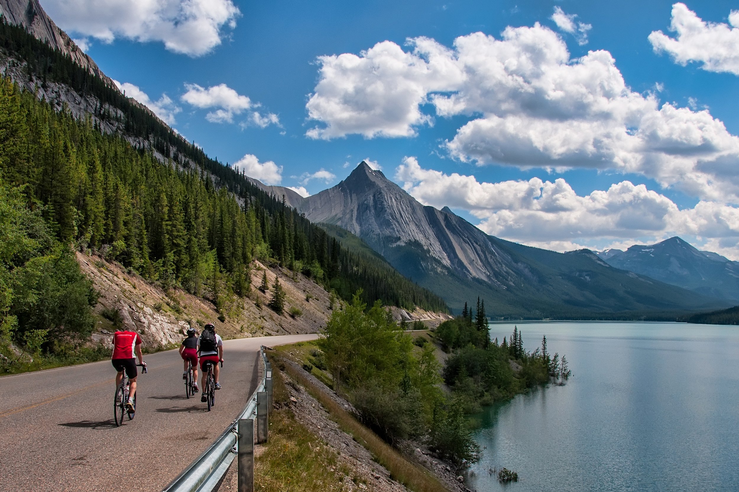 three cyclists on a road in Jasper national park with a mountain peak in the distance