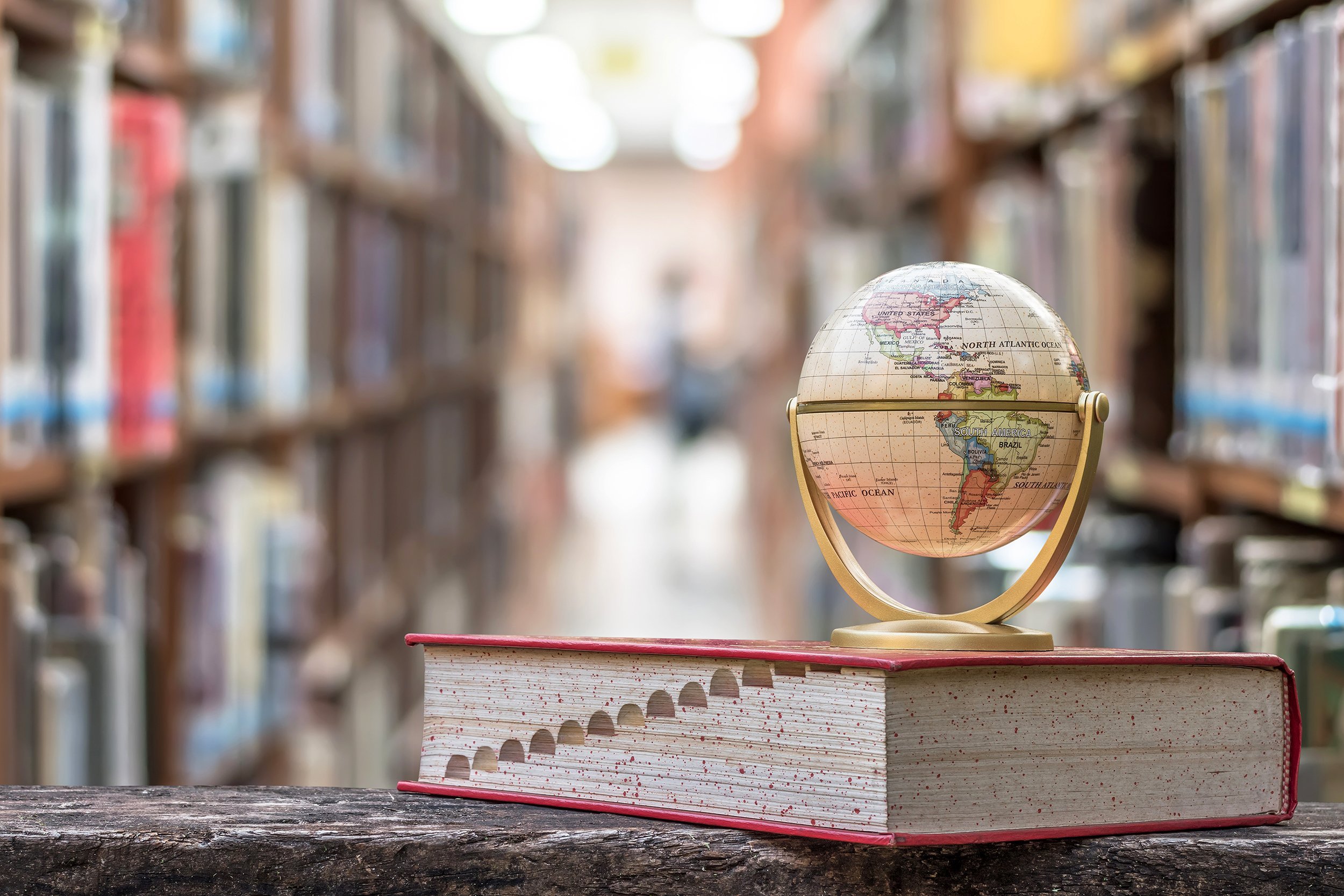Small globe on top of a dictionary in a library