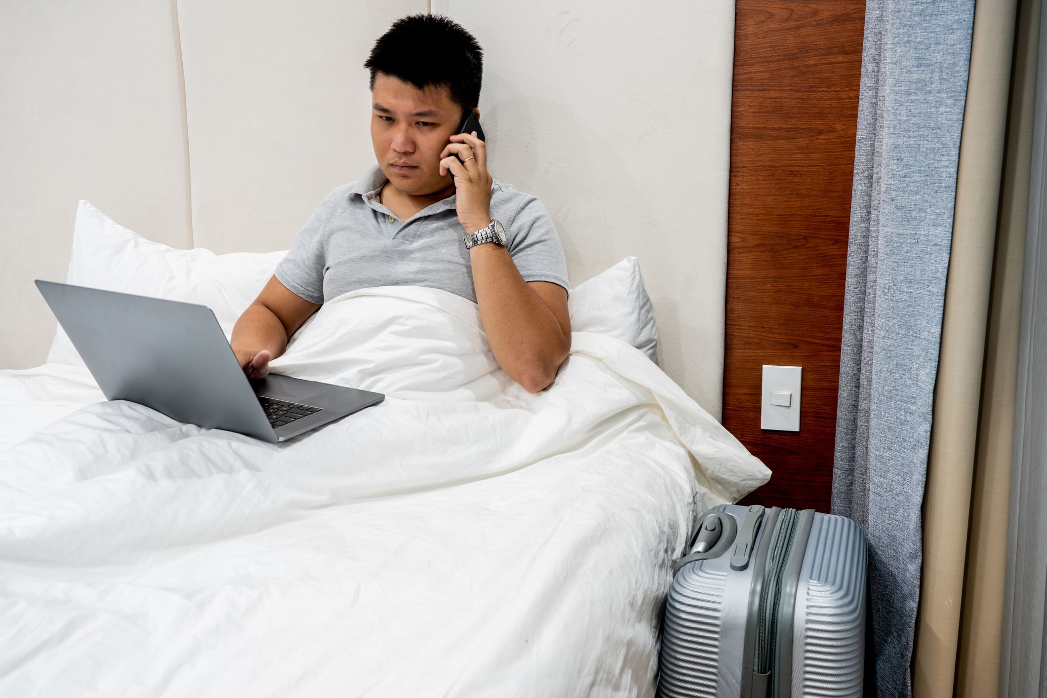 man in hotel bed looking angry calling on phone