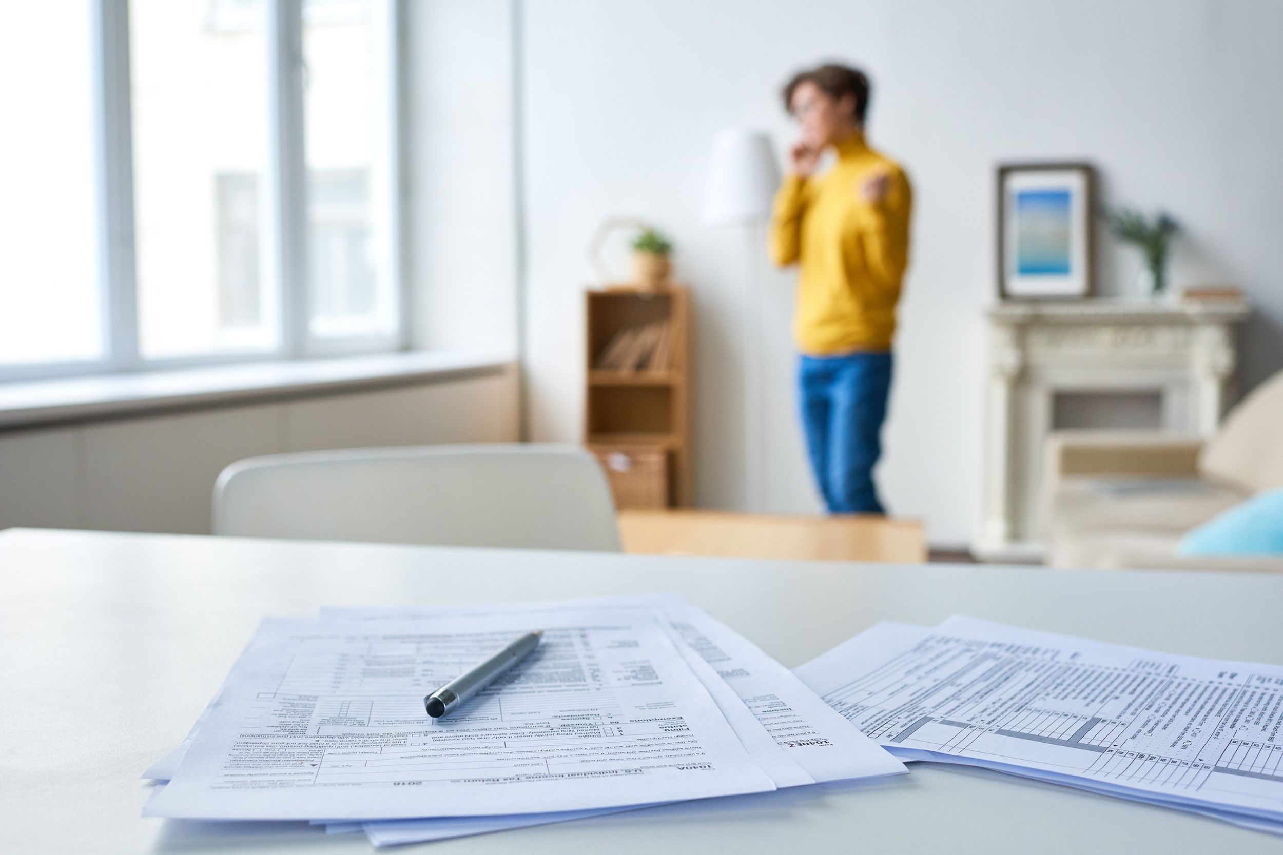 person on phone in background with tax forms on table in close-up