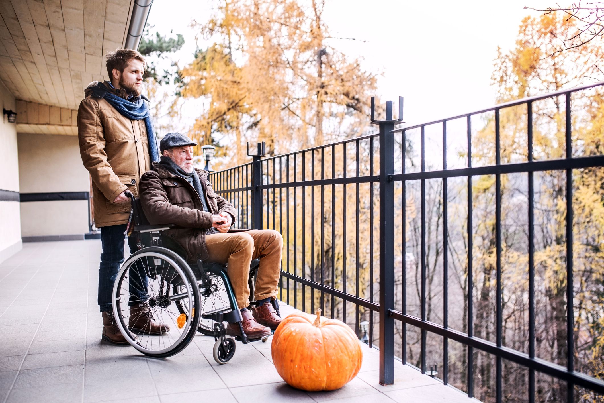 young son and elderly father in wheelchair looking over balcony fence