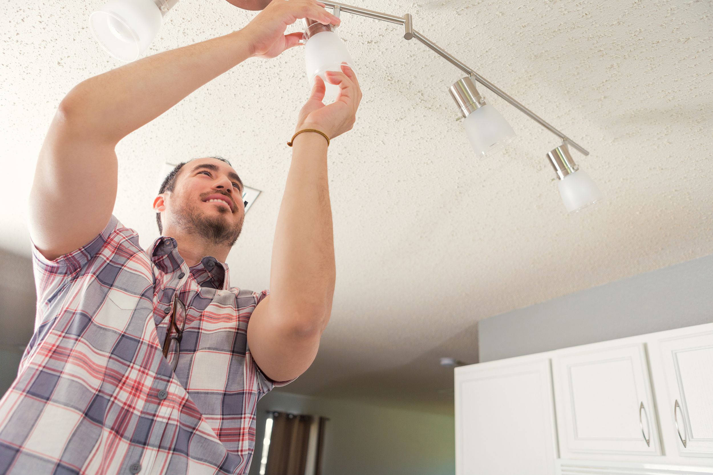 confident man putting lightbulb into socket in ceiling light