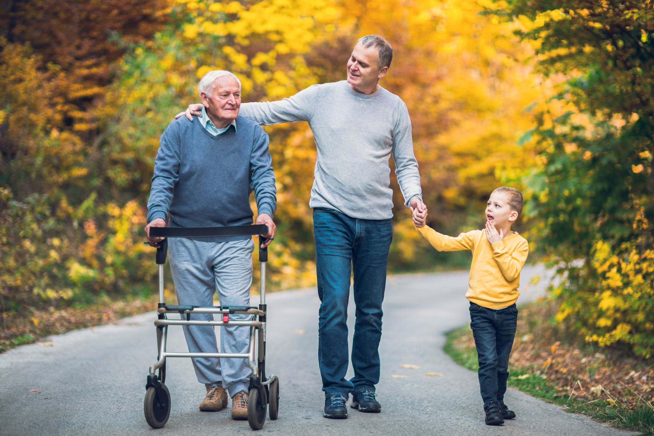 young boy and middle-aged man and senior man with walker walking through park together