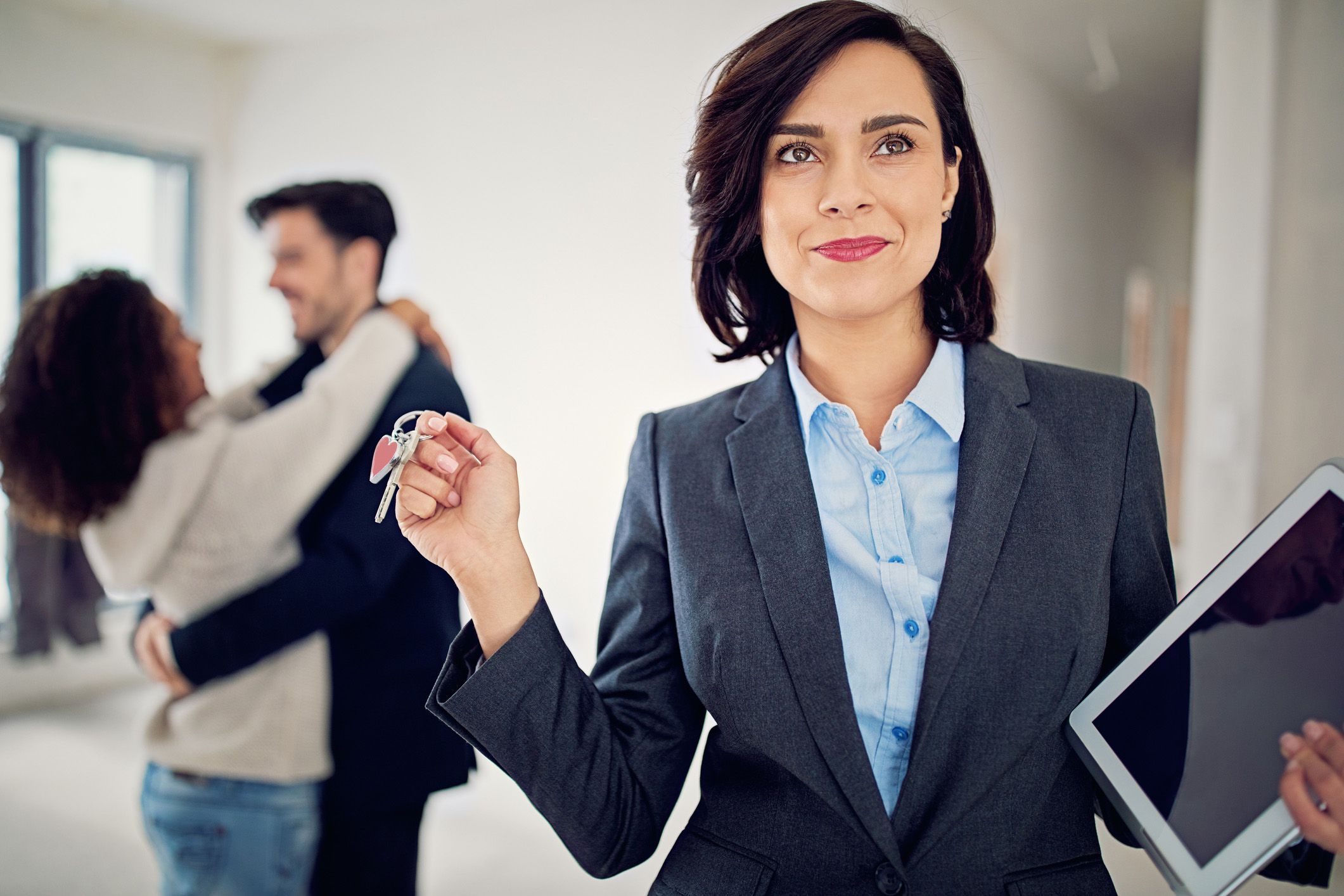 realtor smiling holding keys and documents, happy couple in background