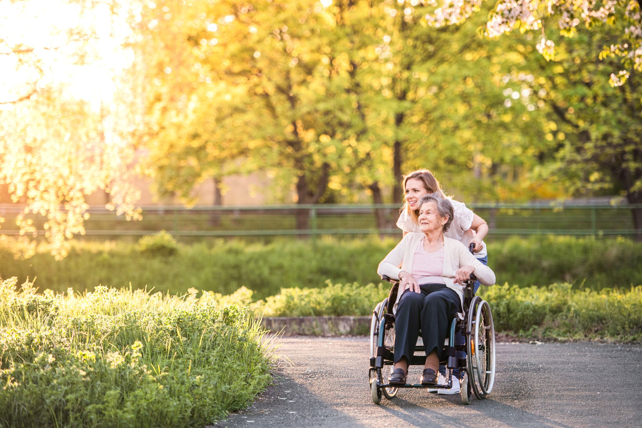 young woman looking at sun and flowers on walk with senior woman in wheelchair