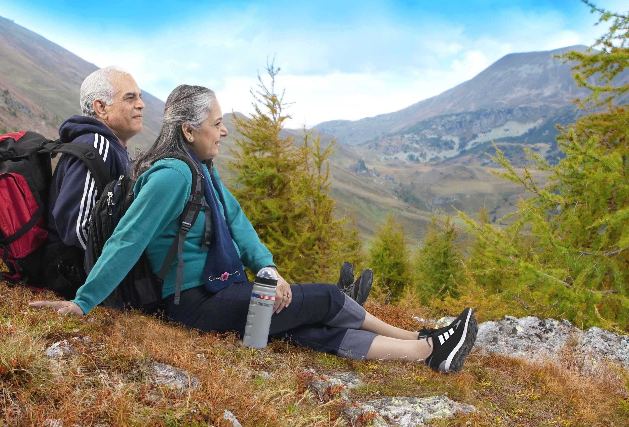Old couple sitting on hill with hiking gear.