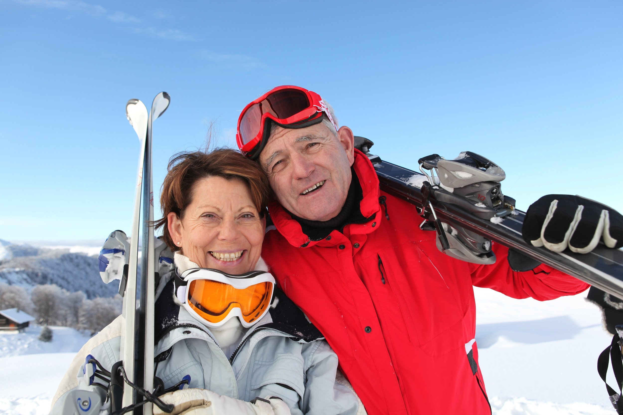 Portrait of a senior man and a senior woman smiling with skis in snow.