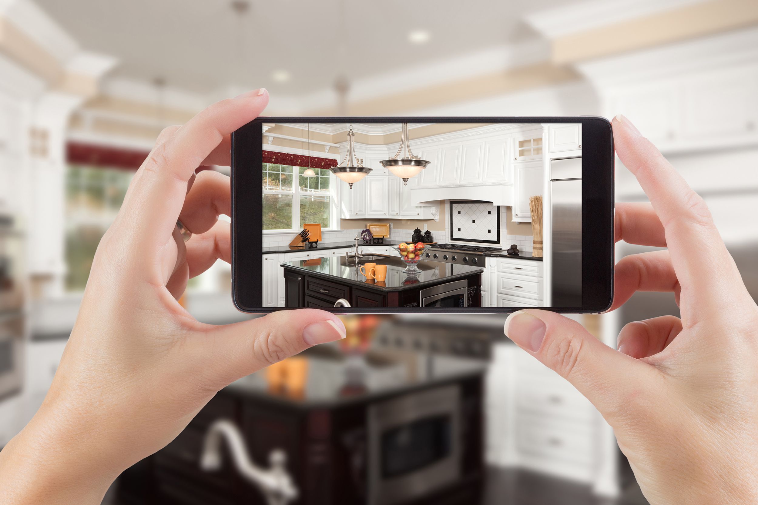 female hands holding smart phone displaying photo of kitchen behind