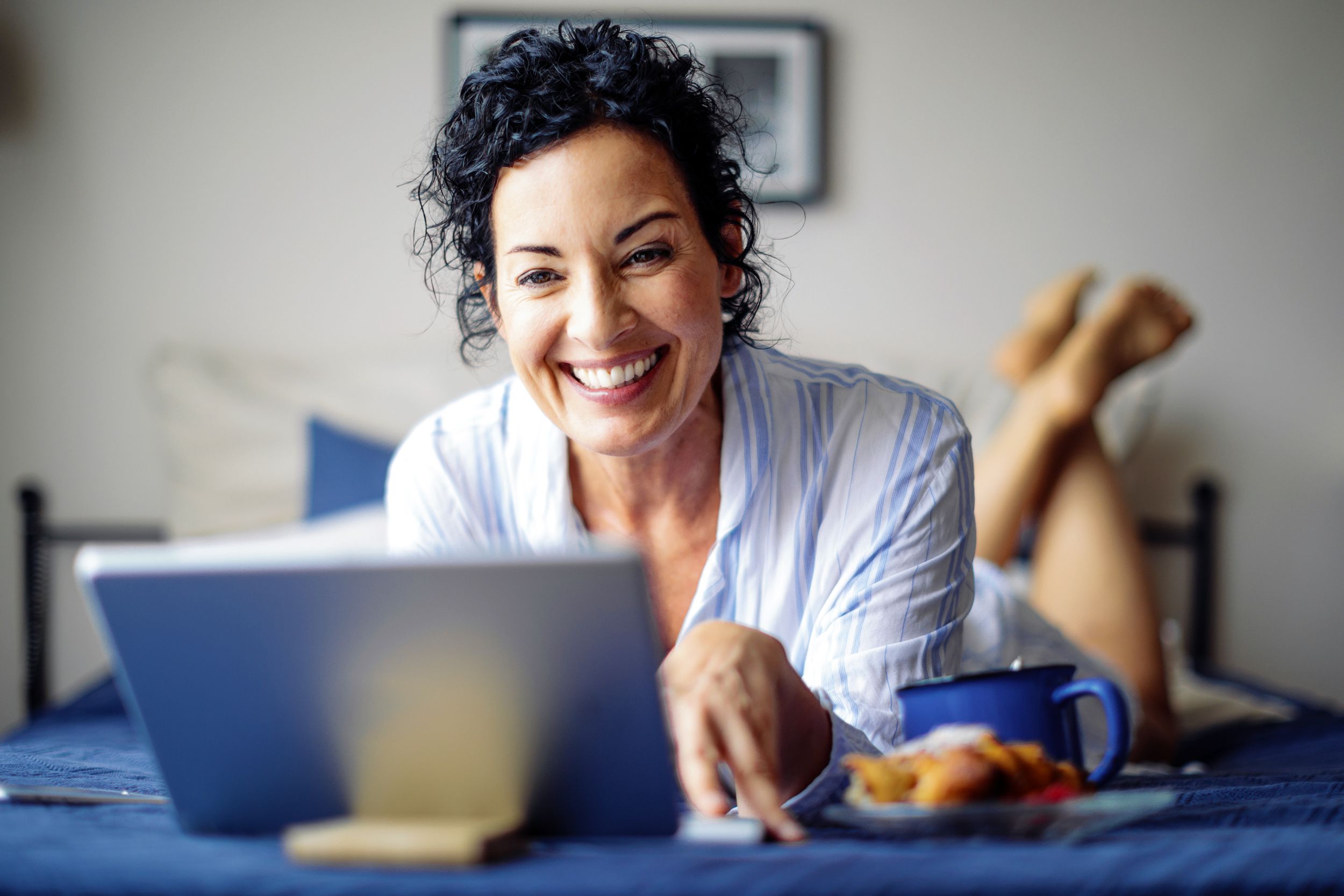 middle-aged woman laying on bed, on laptop