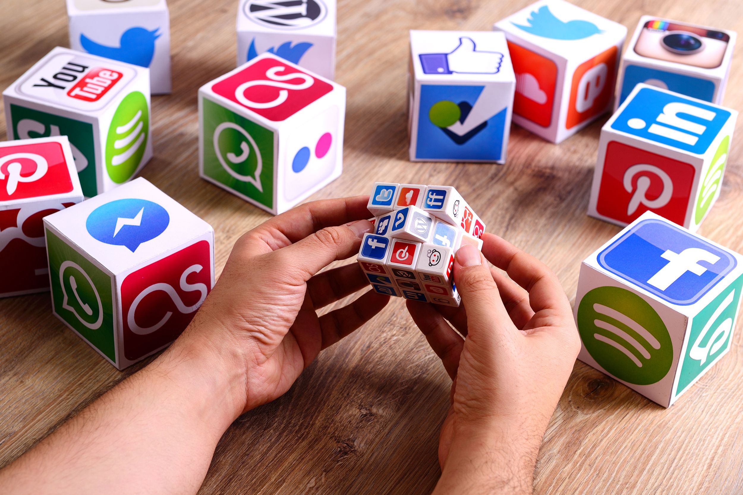 hands holding a Rubik's Cube covered by social media icons on a wooden desk
