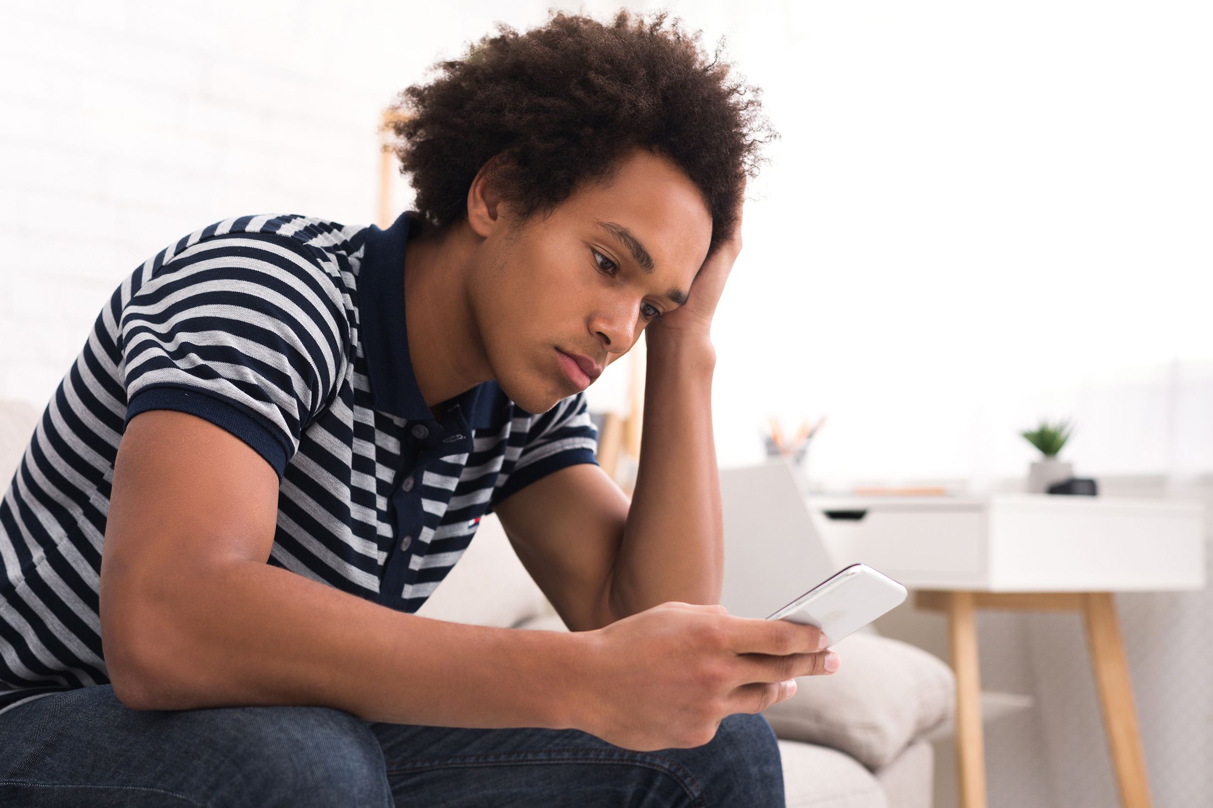depressed teenage boy looking at his smartphone
