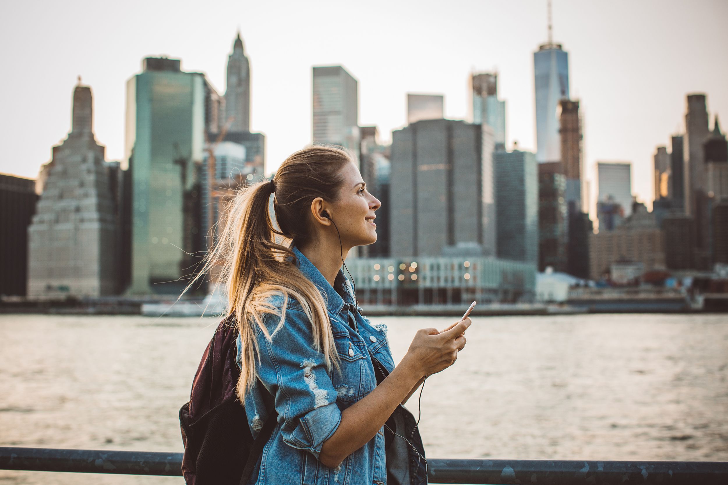 young woman walking along water edge with downtown Manhattan in the background