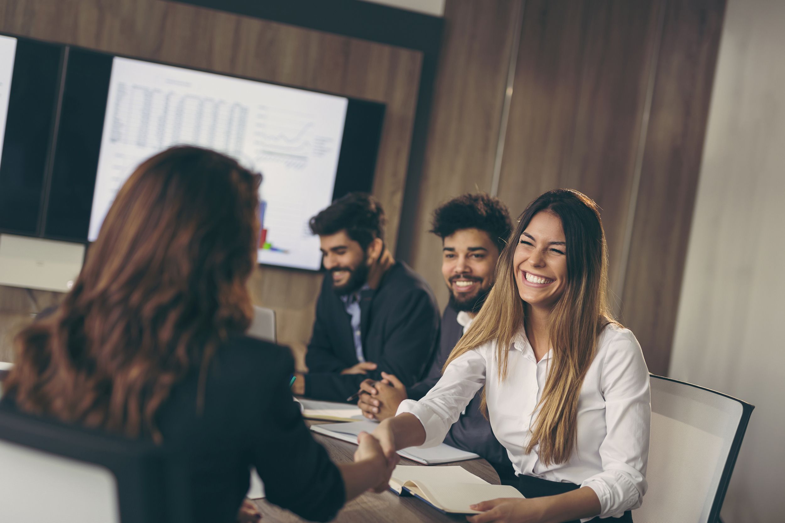woman on job interview shaking hands with another woman, with two guys