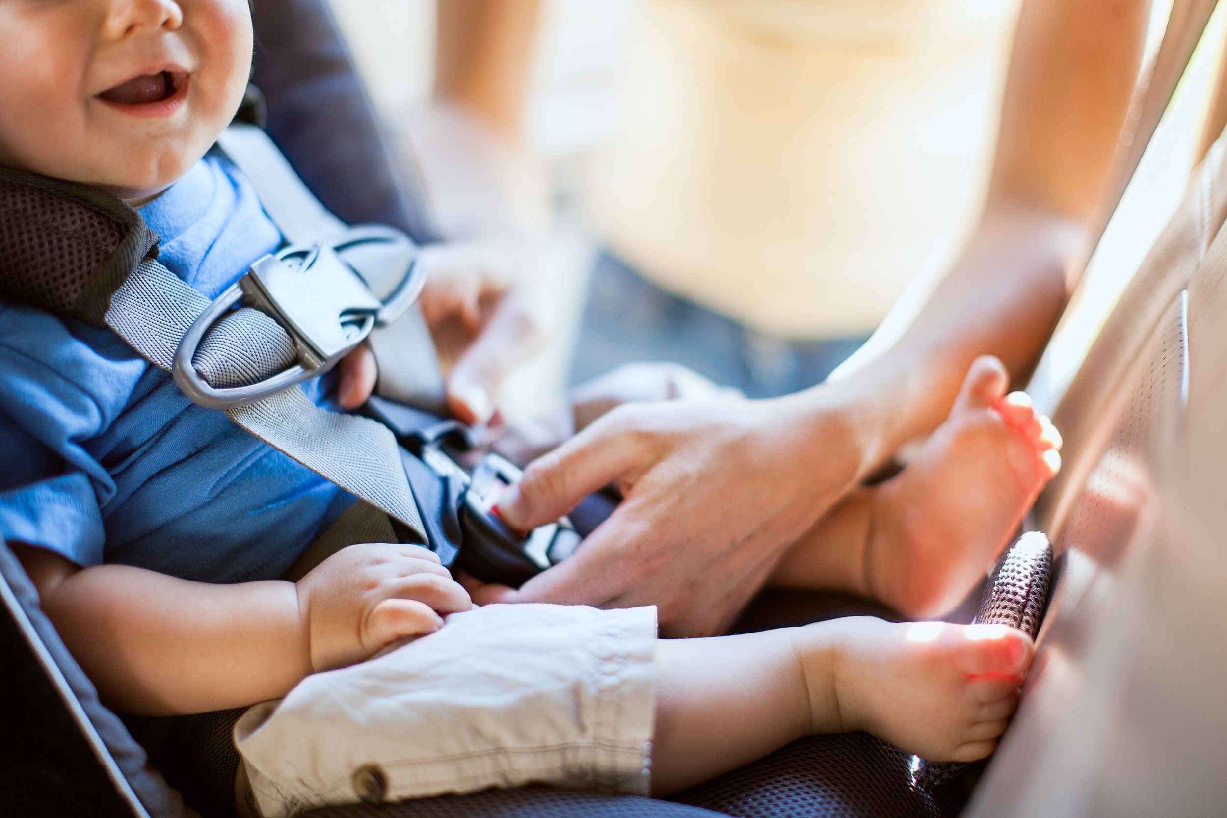 Closeup of mother strapping baby in a carseat, selective focus, blurred background of sunlight coming through opened car door