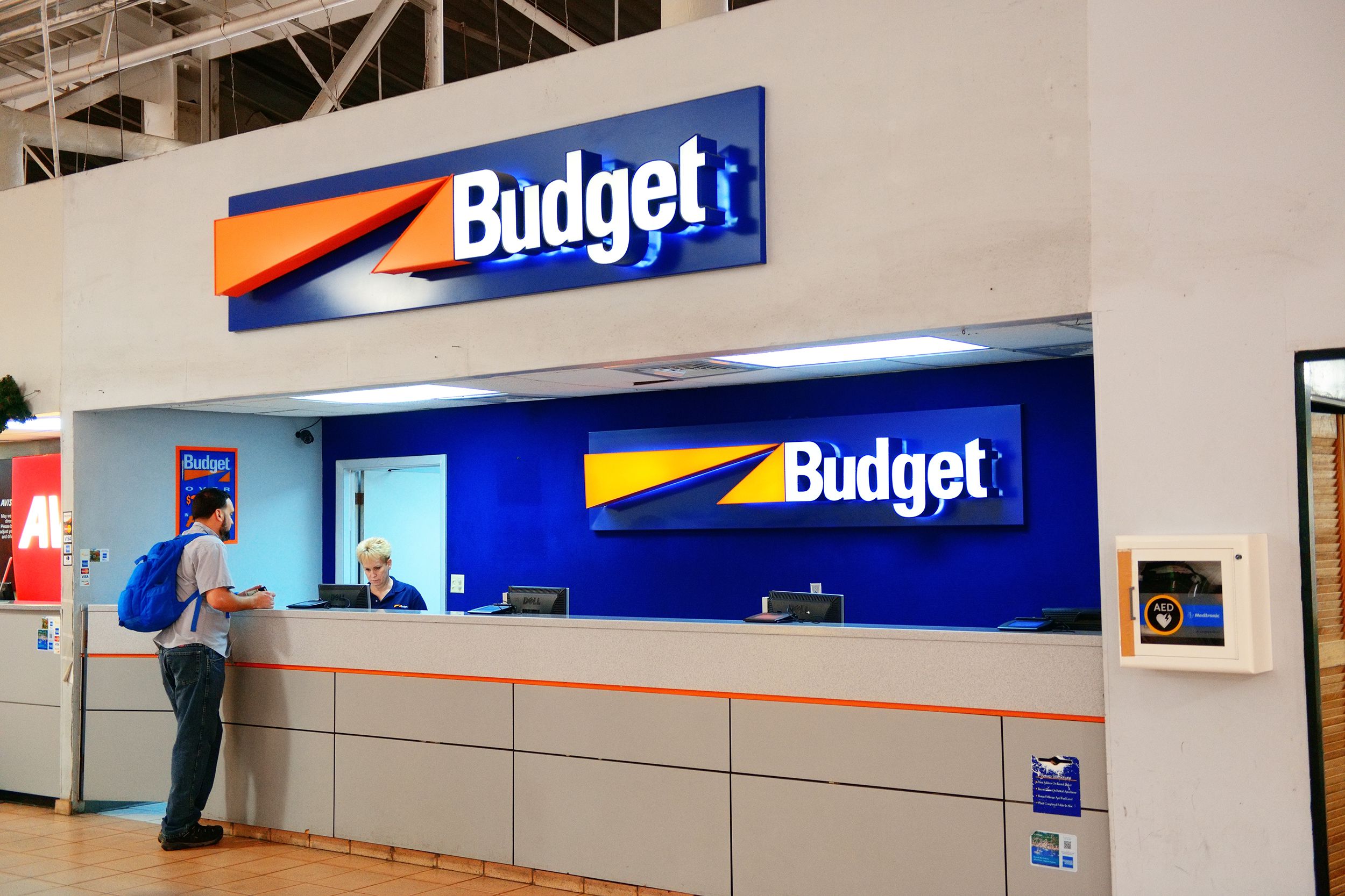 Customer at the counter of a Budget Rent a Car, agent behind counter helping customer, clean and loft ceiling