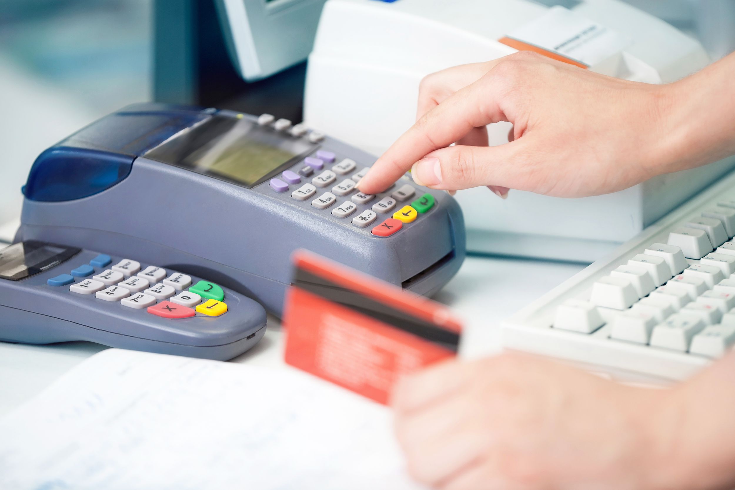 Hands using credit card reader for a transaction at a store, selective focus, on a counter with papers and a computer, blurred