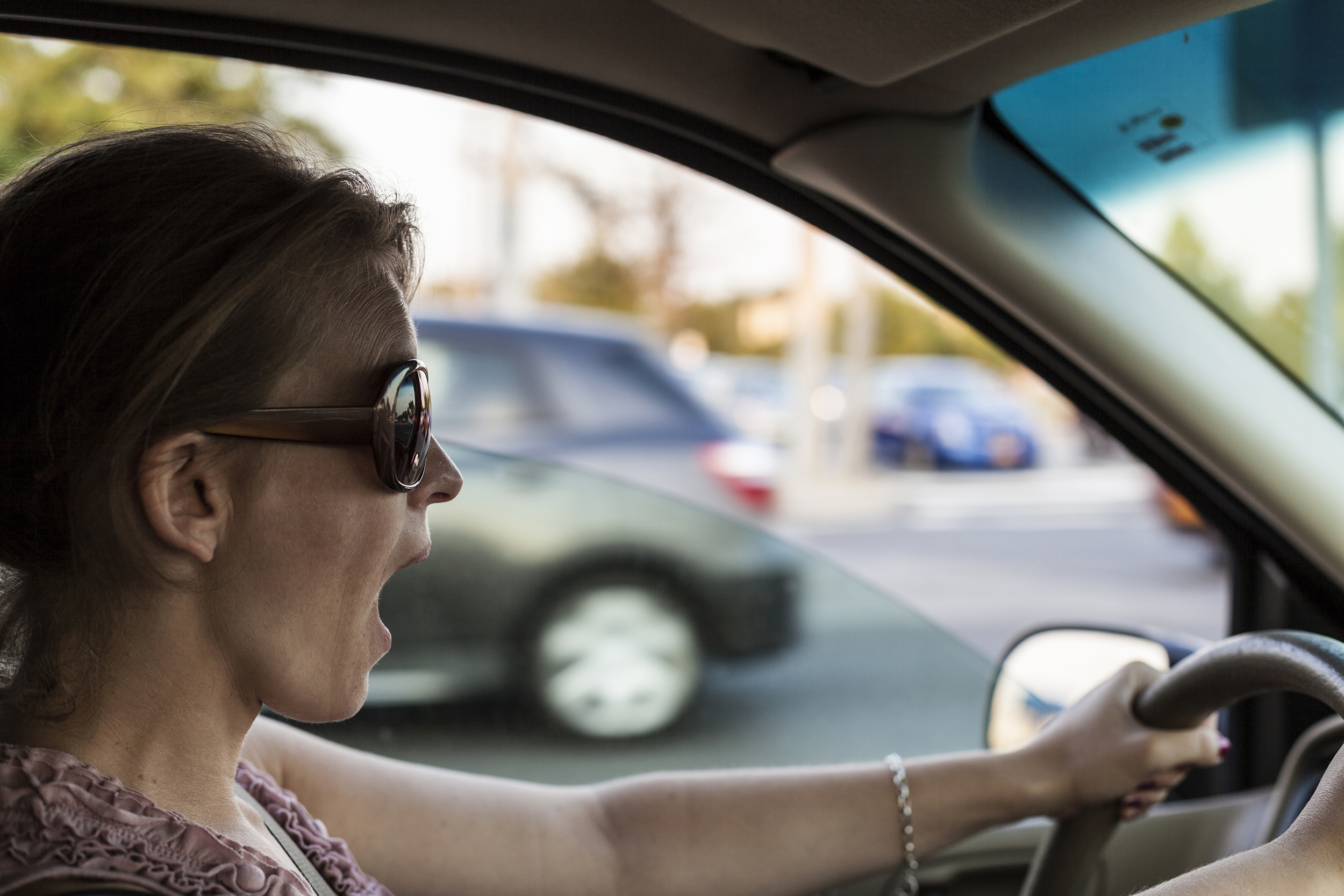 Shocked woman driving a car right before a crash, selective focus, road with cars going in the different direction blurred in the background