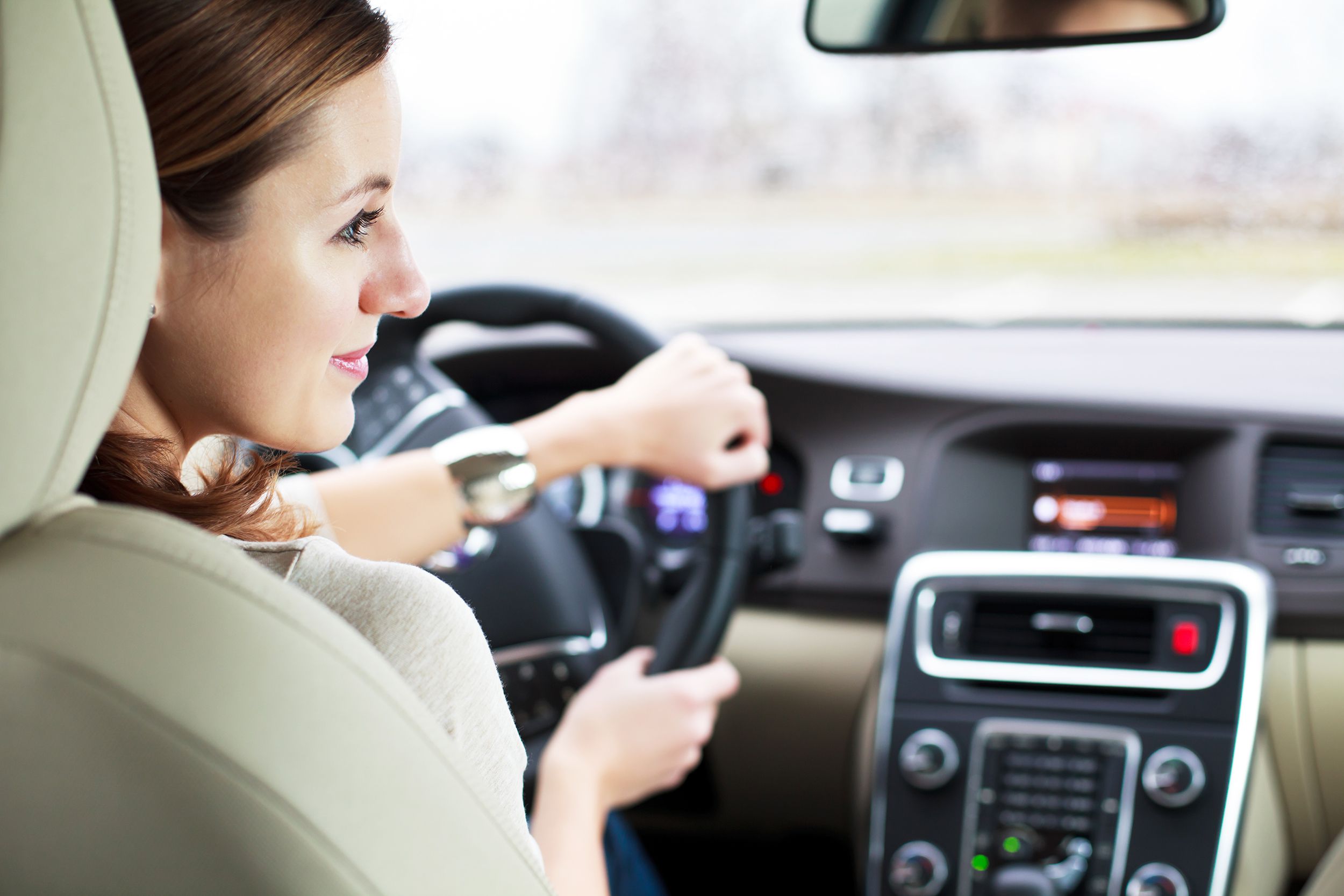 Woman driving a car seen from the backseat, she is turning and looking to the right, blurred dashboard and scenery through the windshield