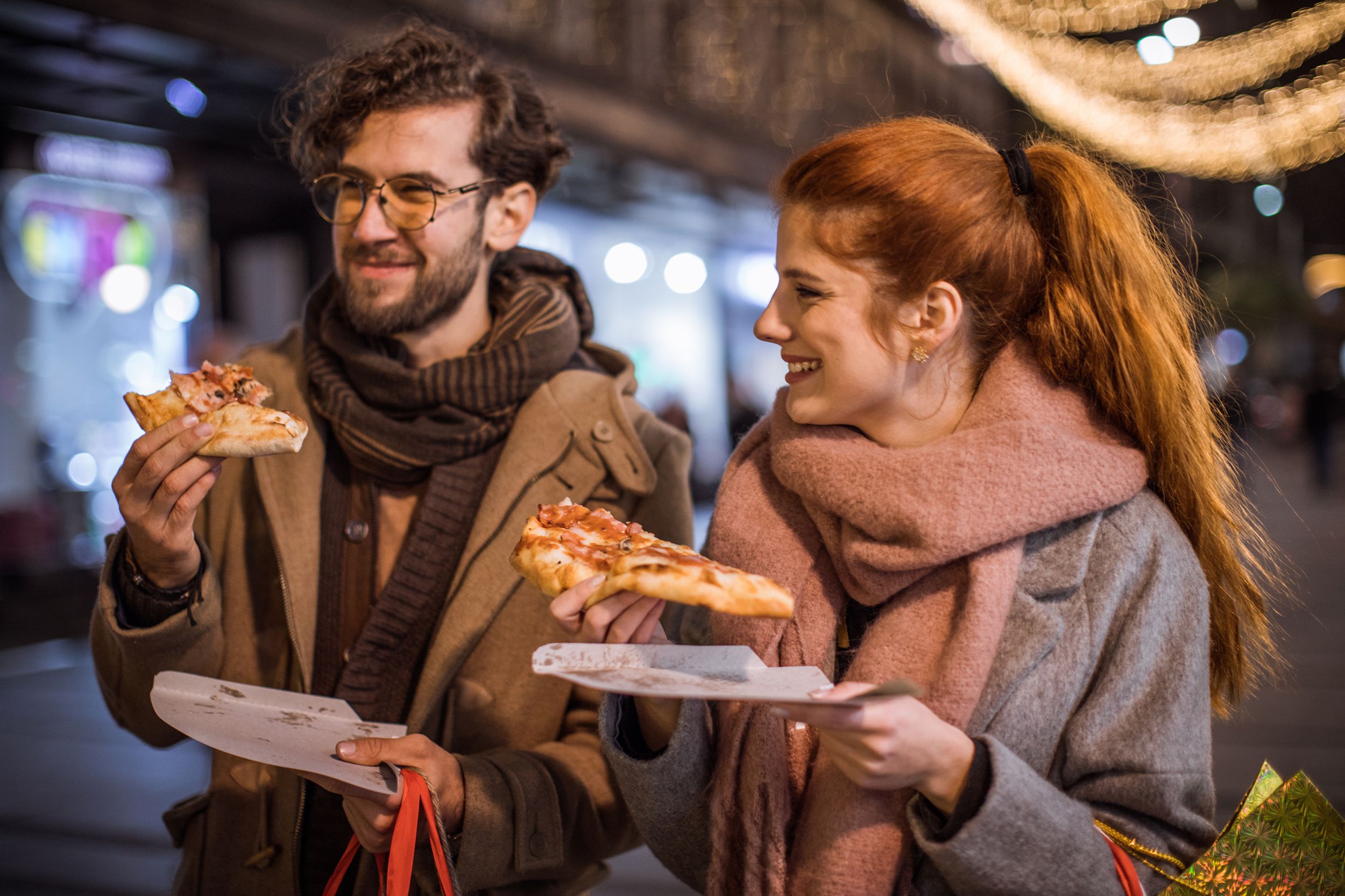 couple eating slices of pizza while walking on a date