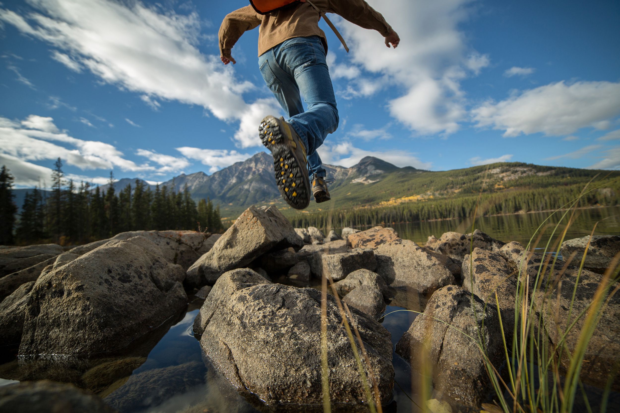 Hiker jumps rock to rock in mountain lake in Jasper National Park, Canada