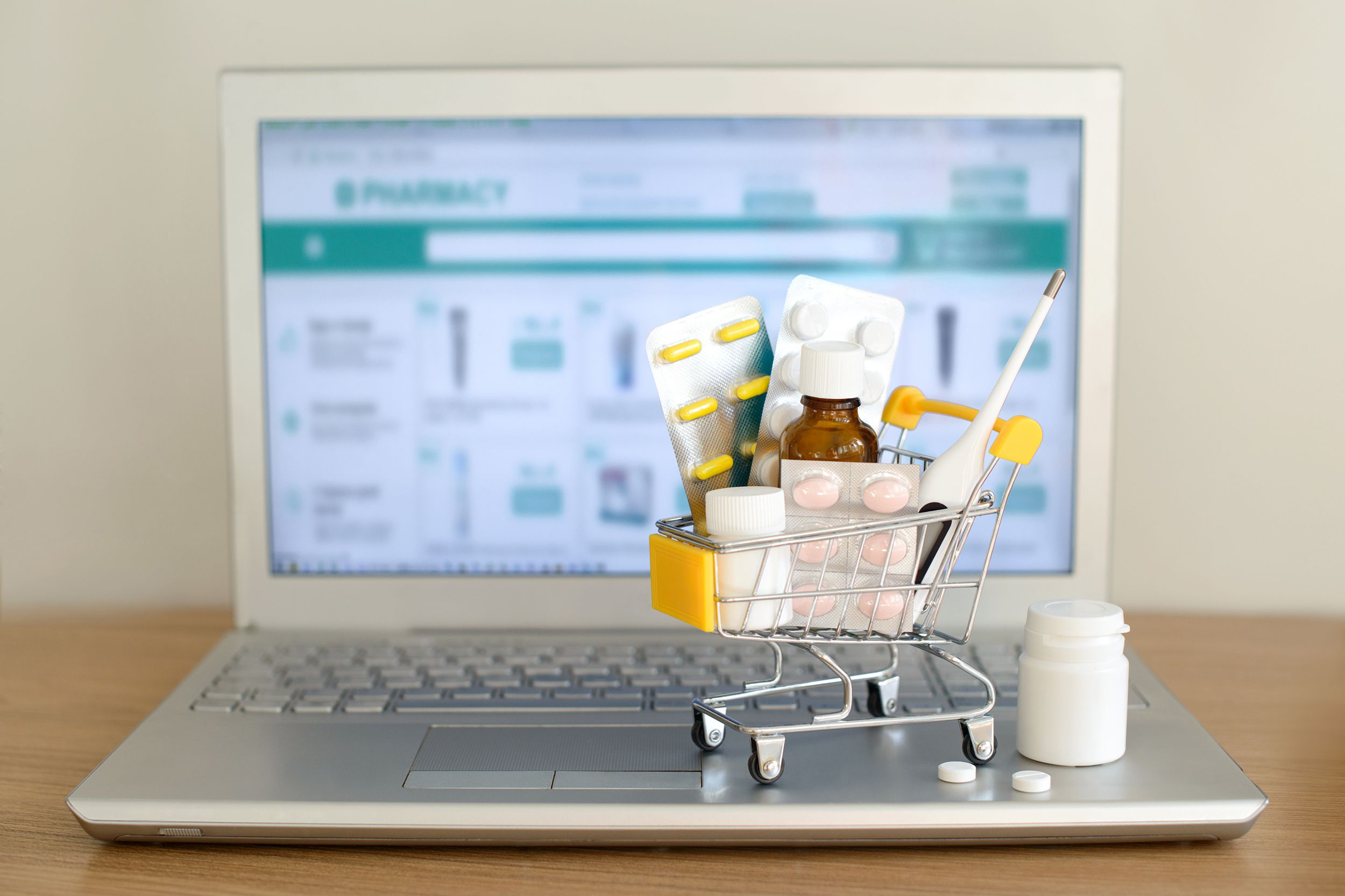 shopping cart toy with medicaments in front of laptop screen with pharmacy web site on it