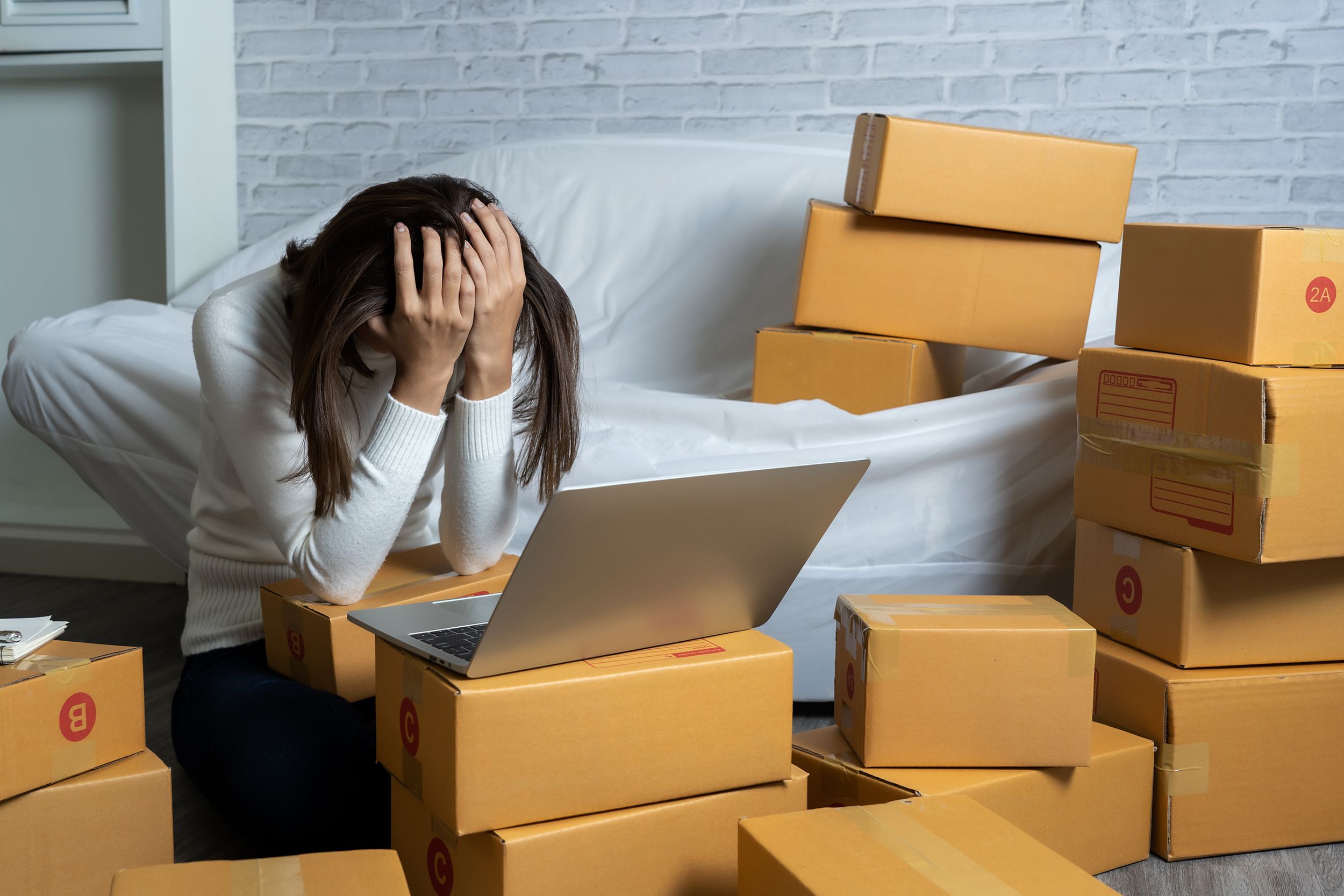 overwhelmed woman with opened laptop selling products at home in boxes