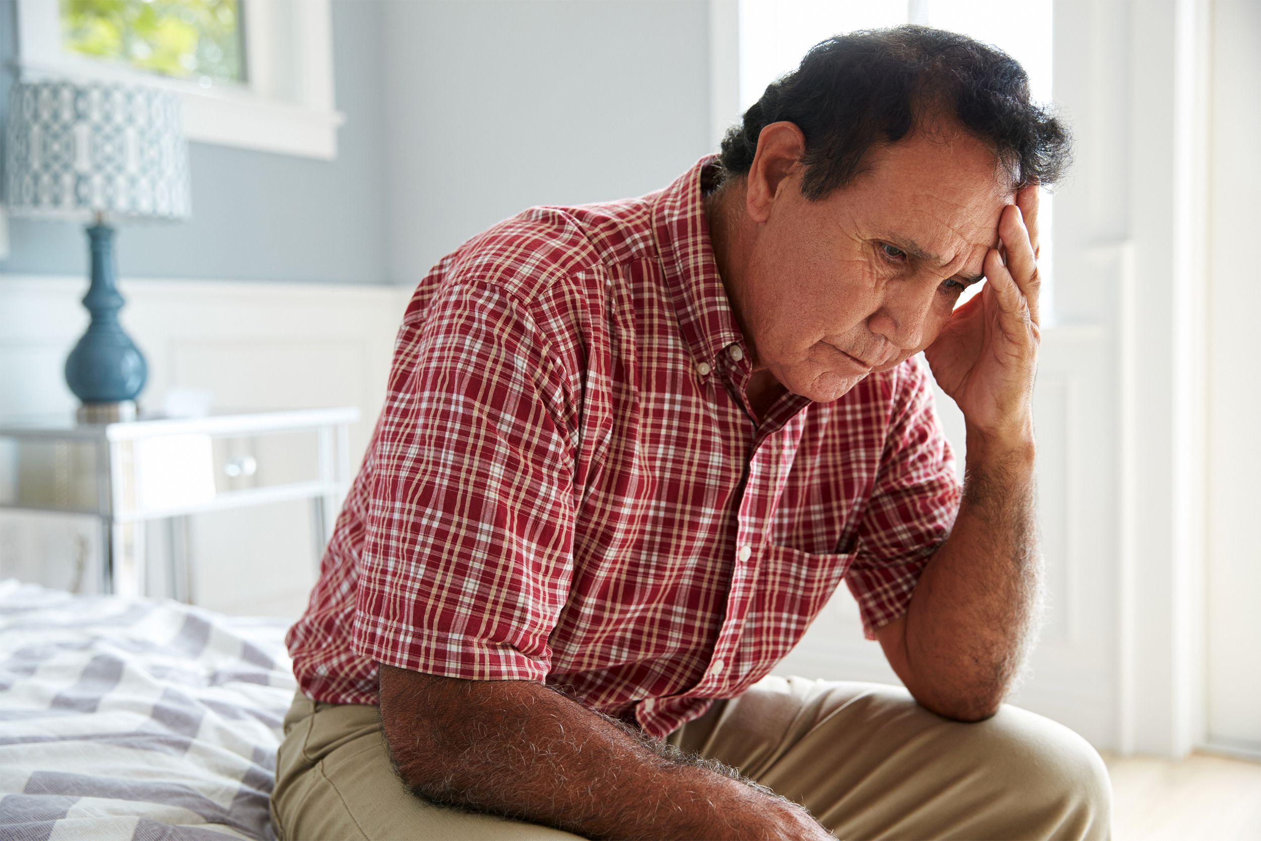 Senior man sitting on the edge of his bed looking distraught