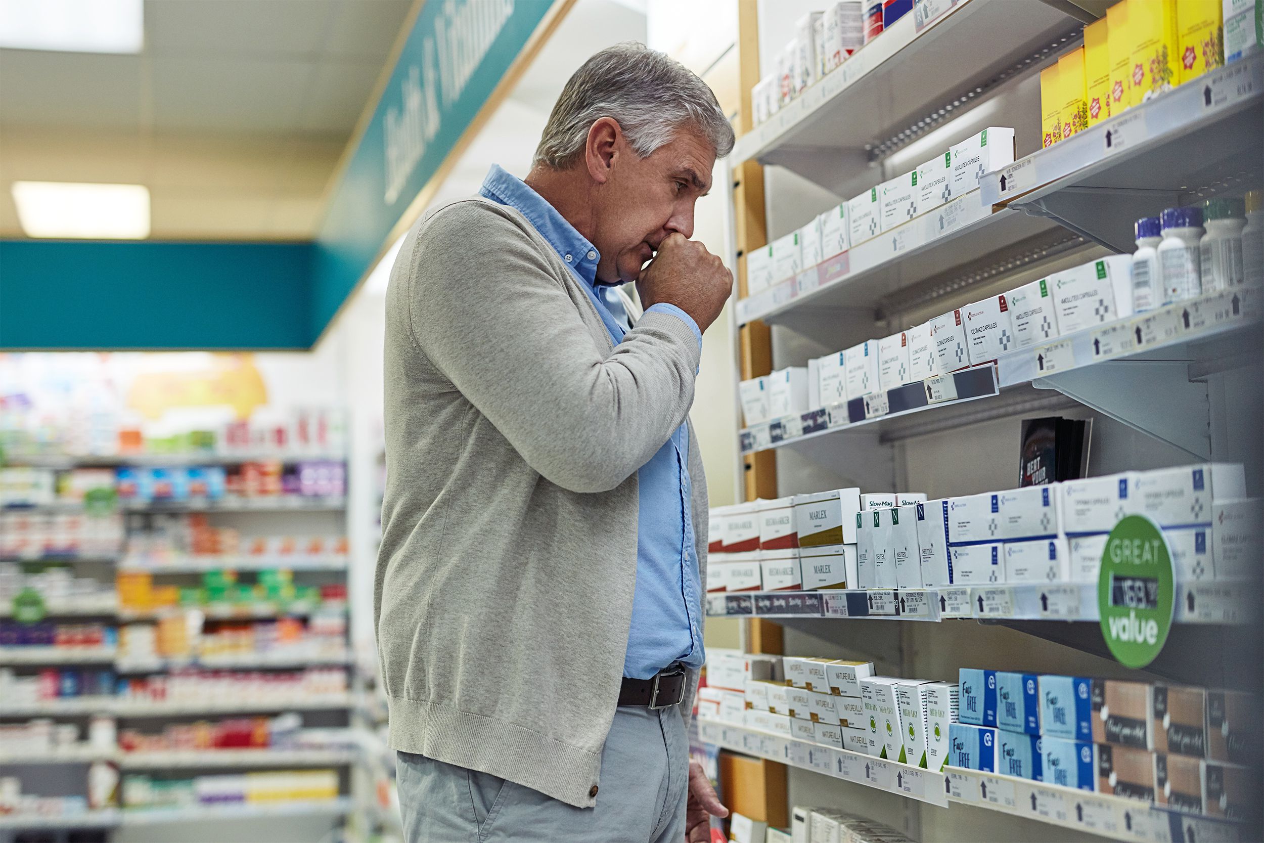 Man coughing in a pharmacy looking at medicine