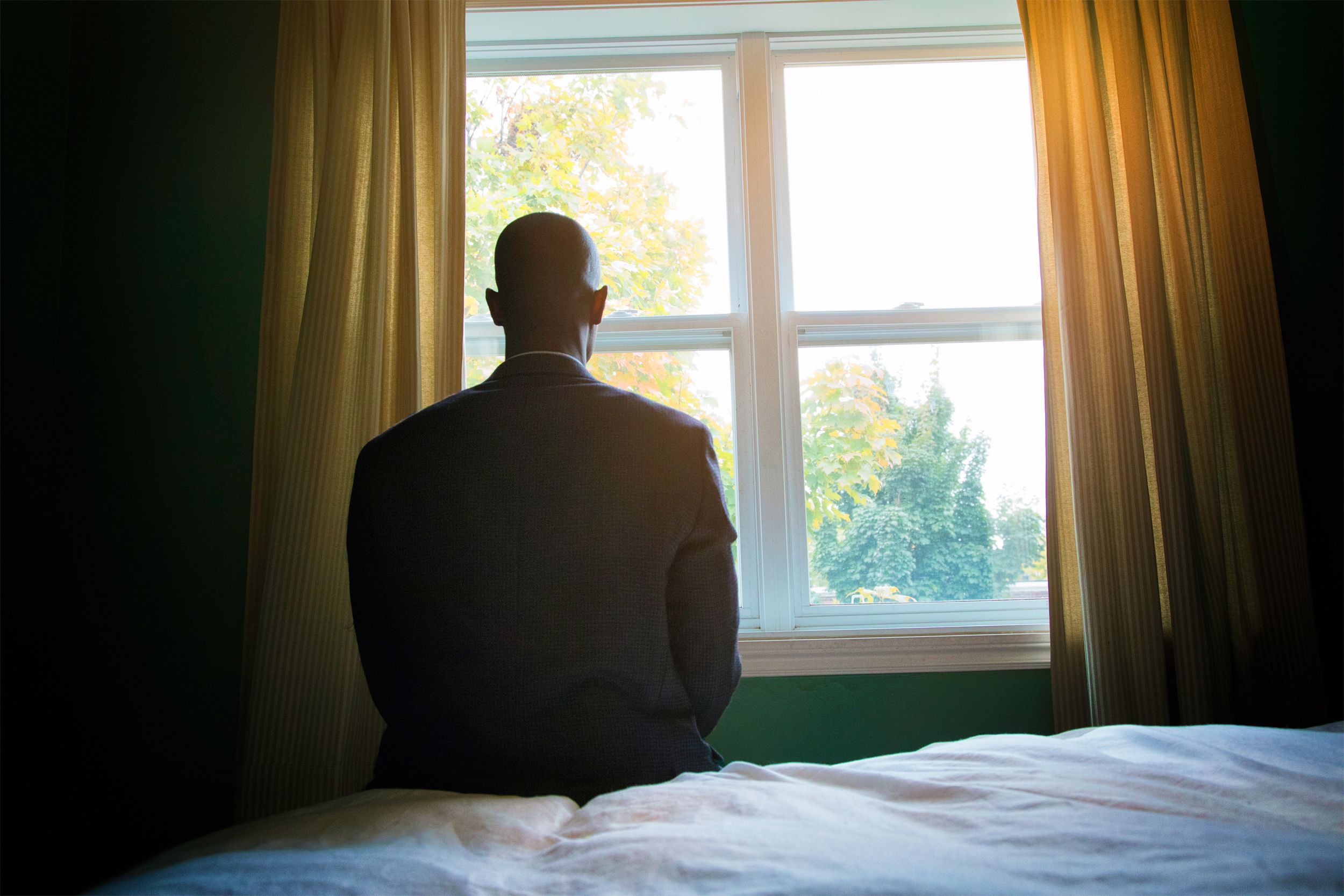 Man sitting on the edge of his bed looking out of the window