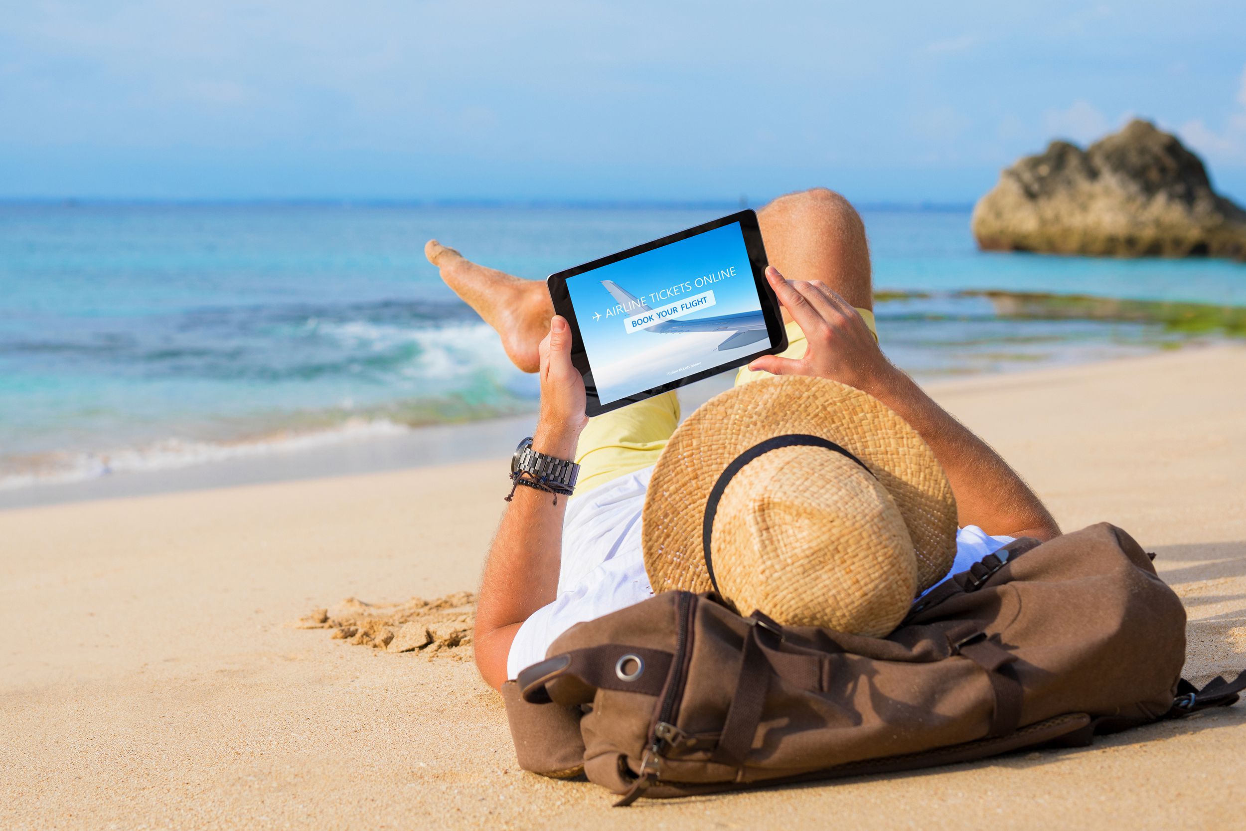 man buying airline tickets online on tablet while relaxing on beach