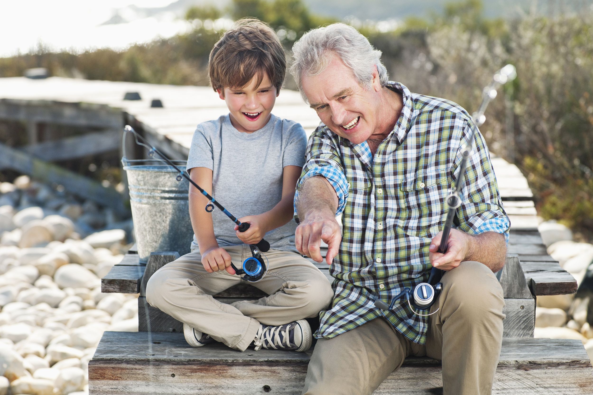 cheerful senior man fishing with boy on pier
