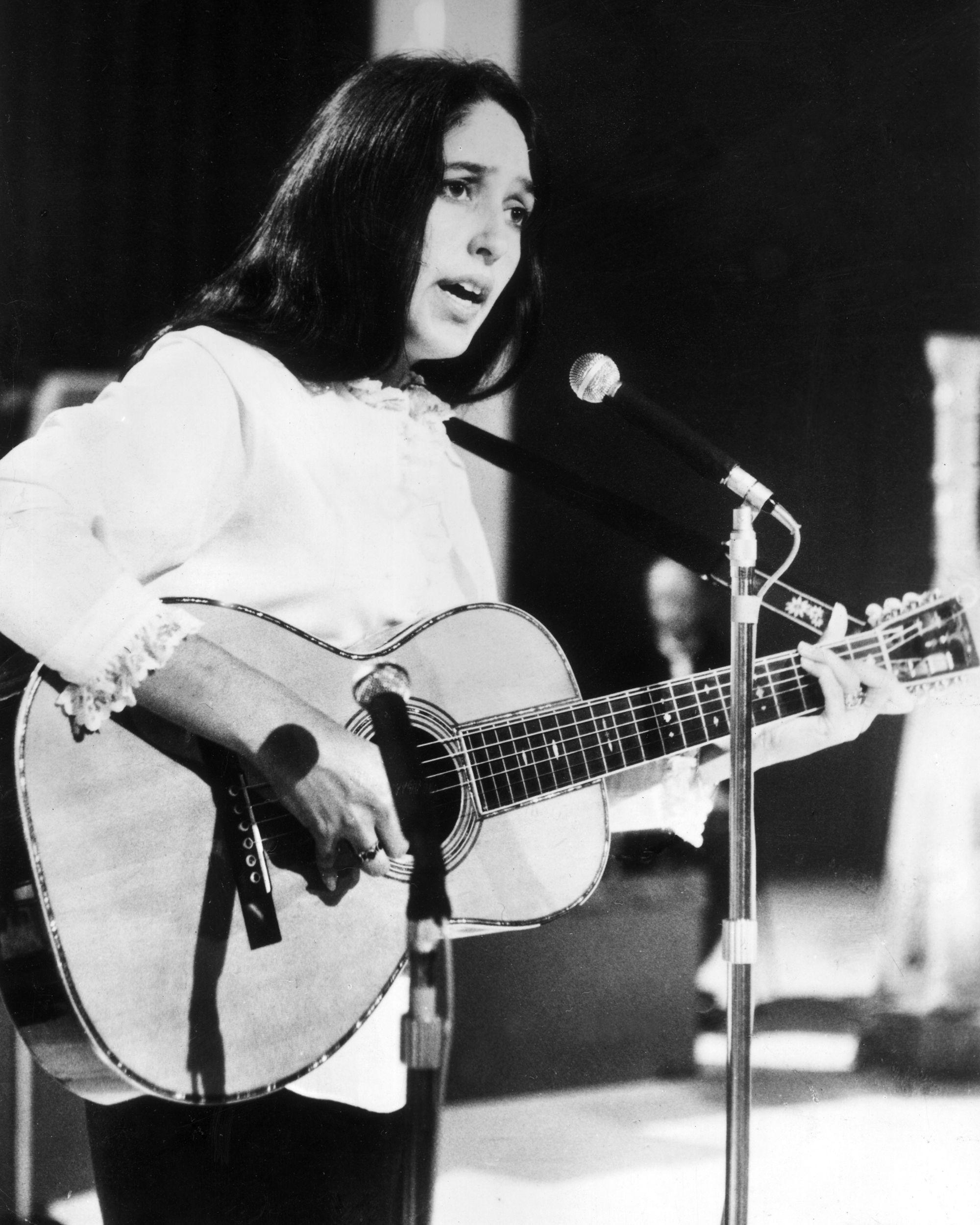 circa 1966: American folk singer Joan Baez sings and plays acoustic guitar on stage during a European tour, East Berlin, Germany