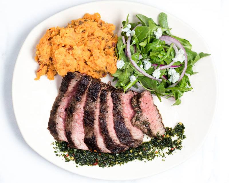 beef, salad, and side on plate with white background