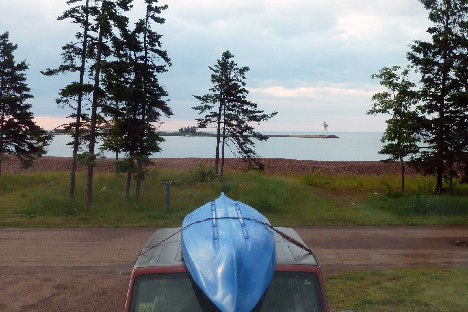 view from rv, canoe on car in foreground, beach and lighthouse and trees in background, in grand marais campground