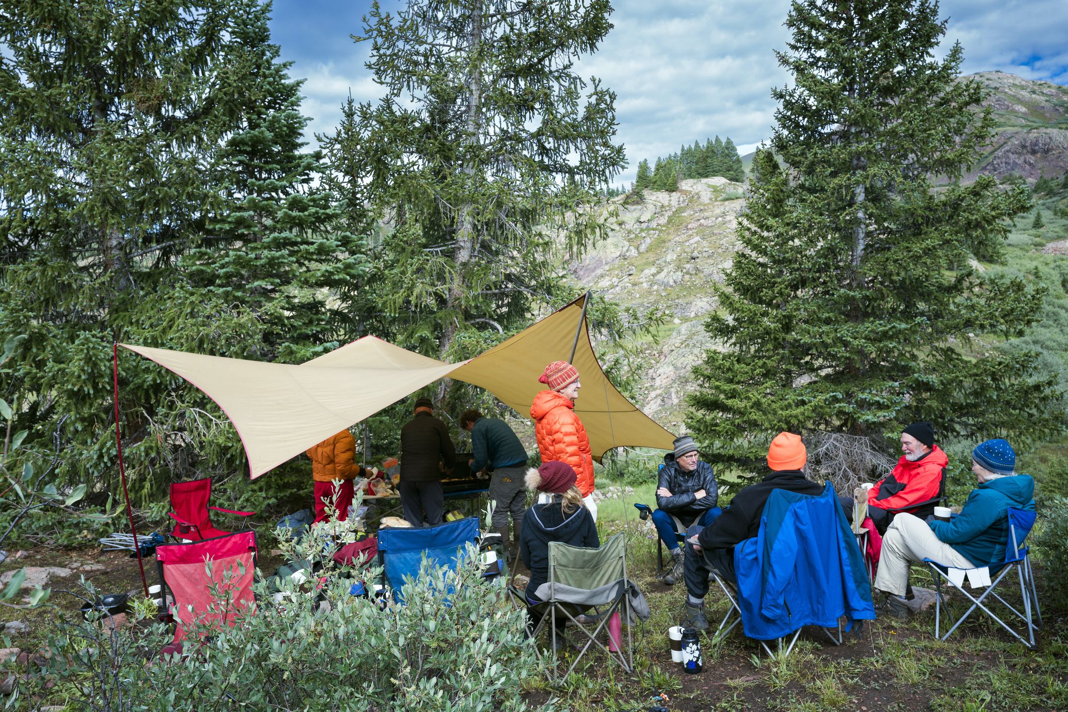 people sitting in foldable chairs below tarp in mountainous area