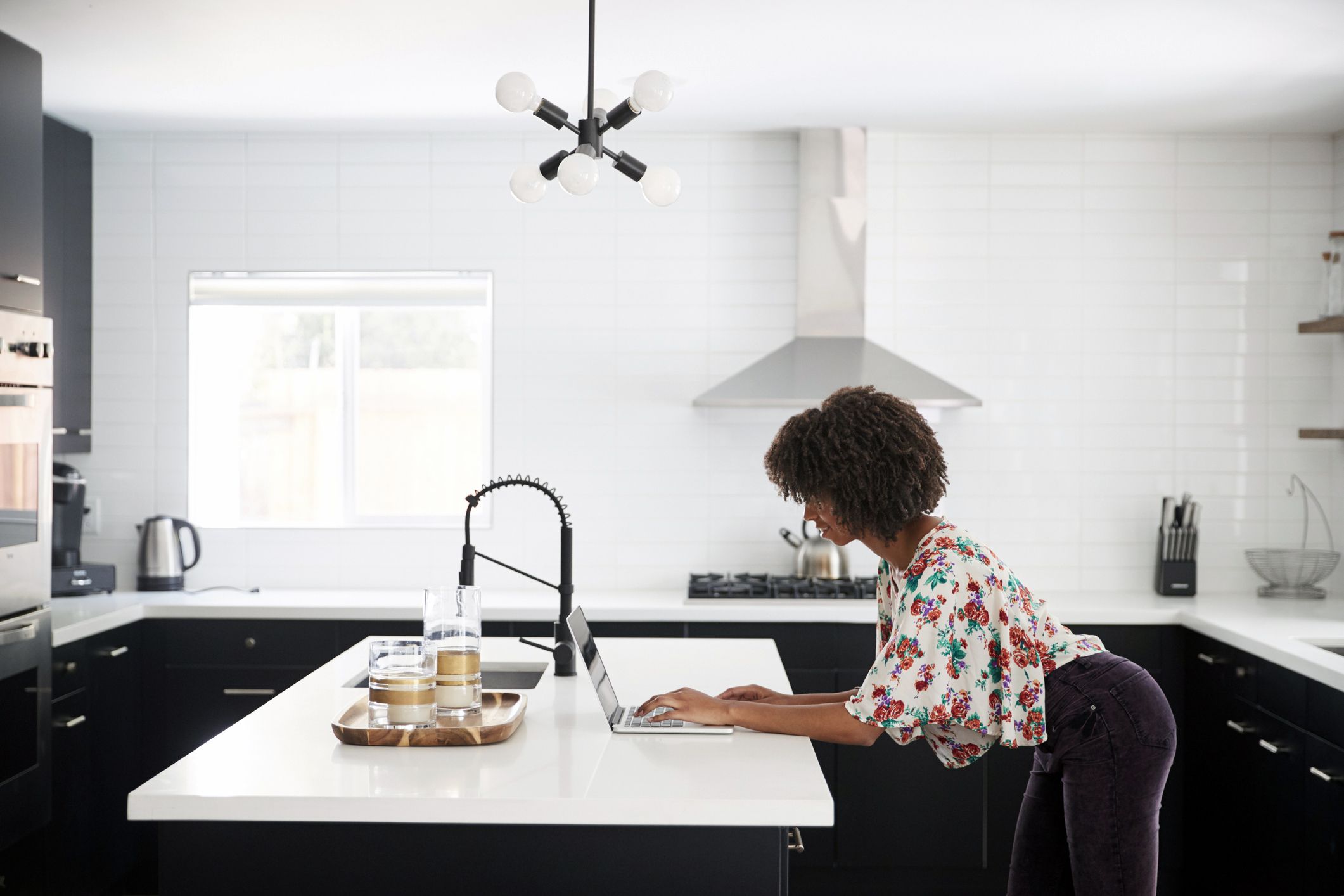woman in kitchen downloading files on computer, standing, on her way out