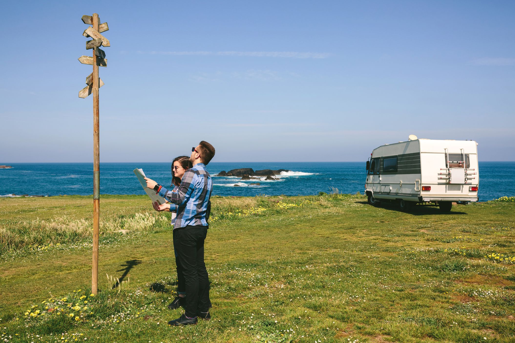 couple standing outside rv on shoreline looking at trail signs