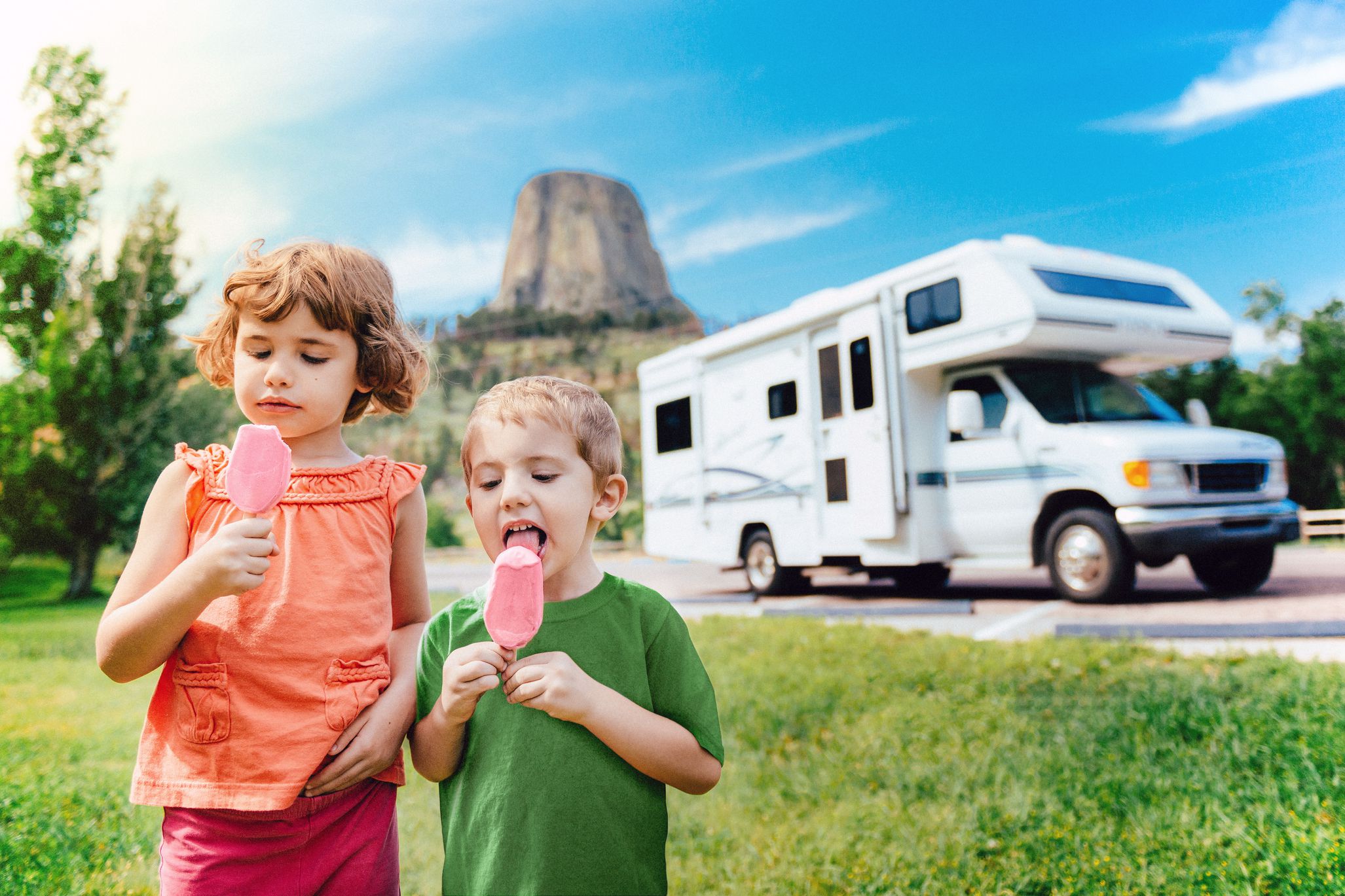 two children walking in grass eating ice cream, rv in distance
