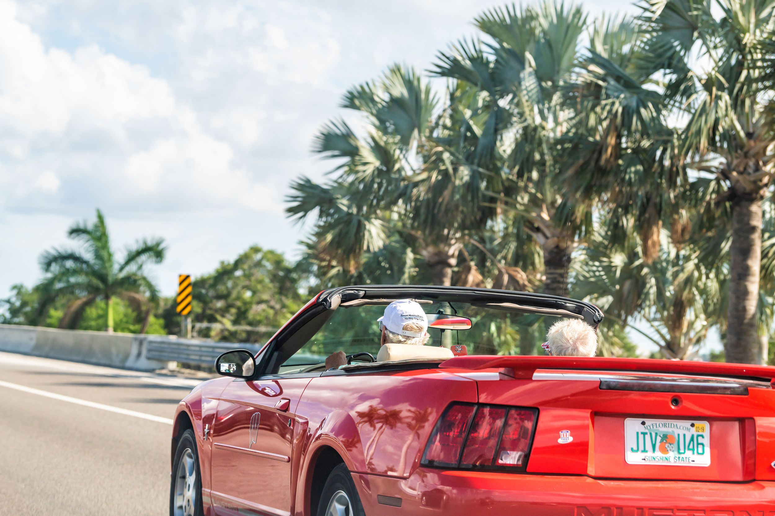senior couple driving on sports car on road, highway with palm trees in Florida