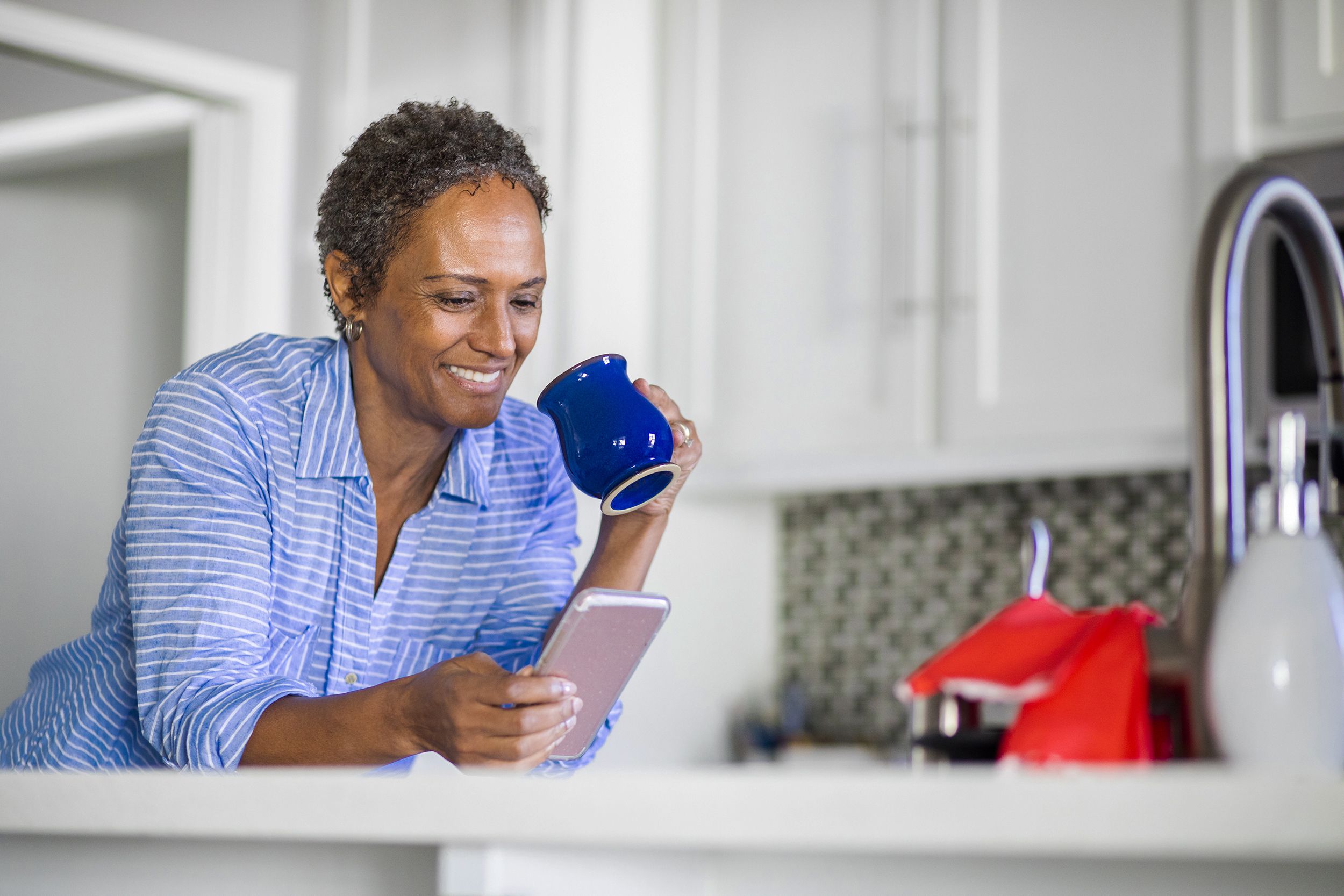 senior woman with cell phone, drinking coffee in kitchen