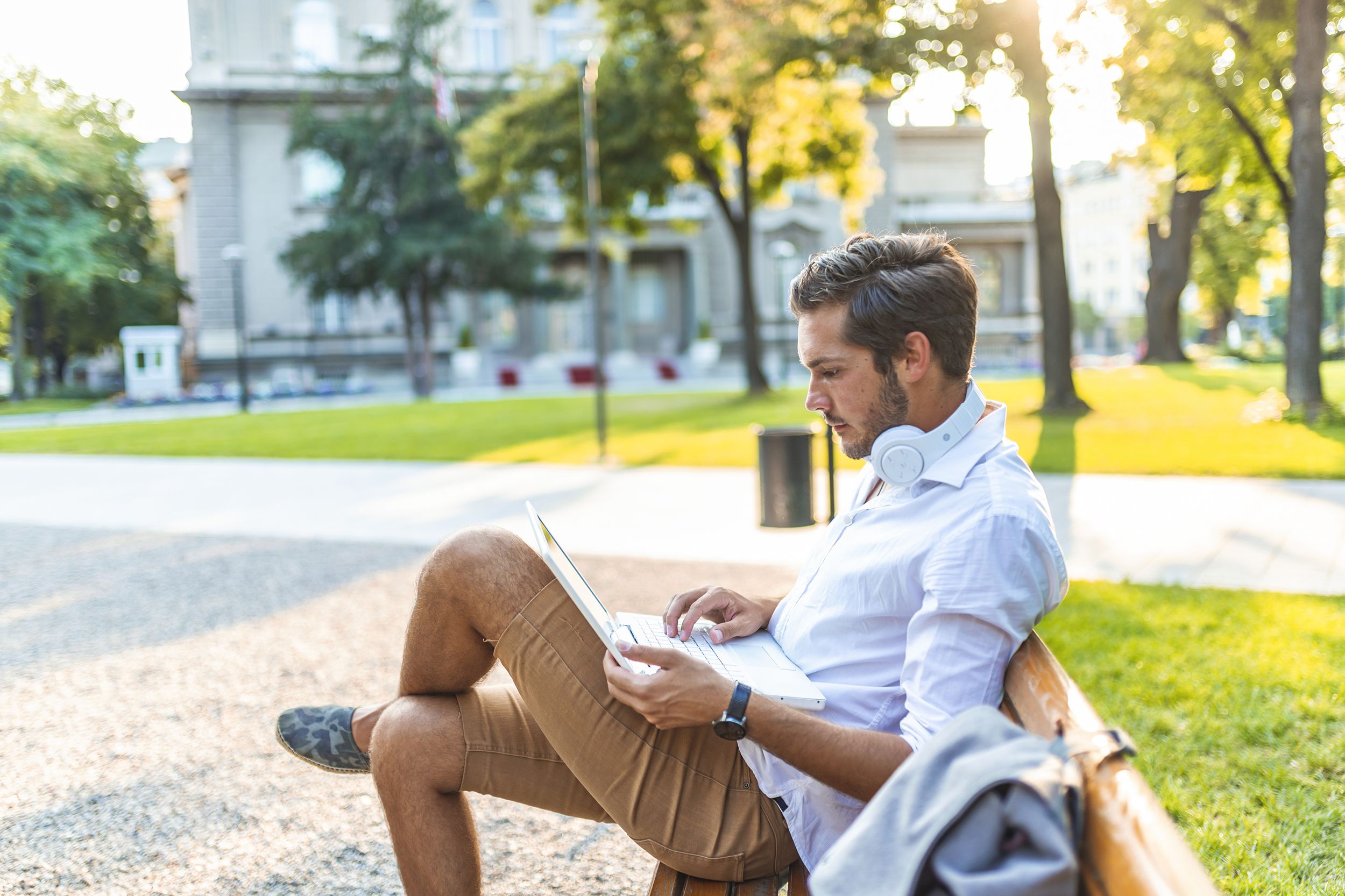 happy man sitting on bench and using laptop in a park