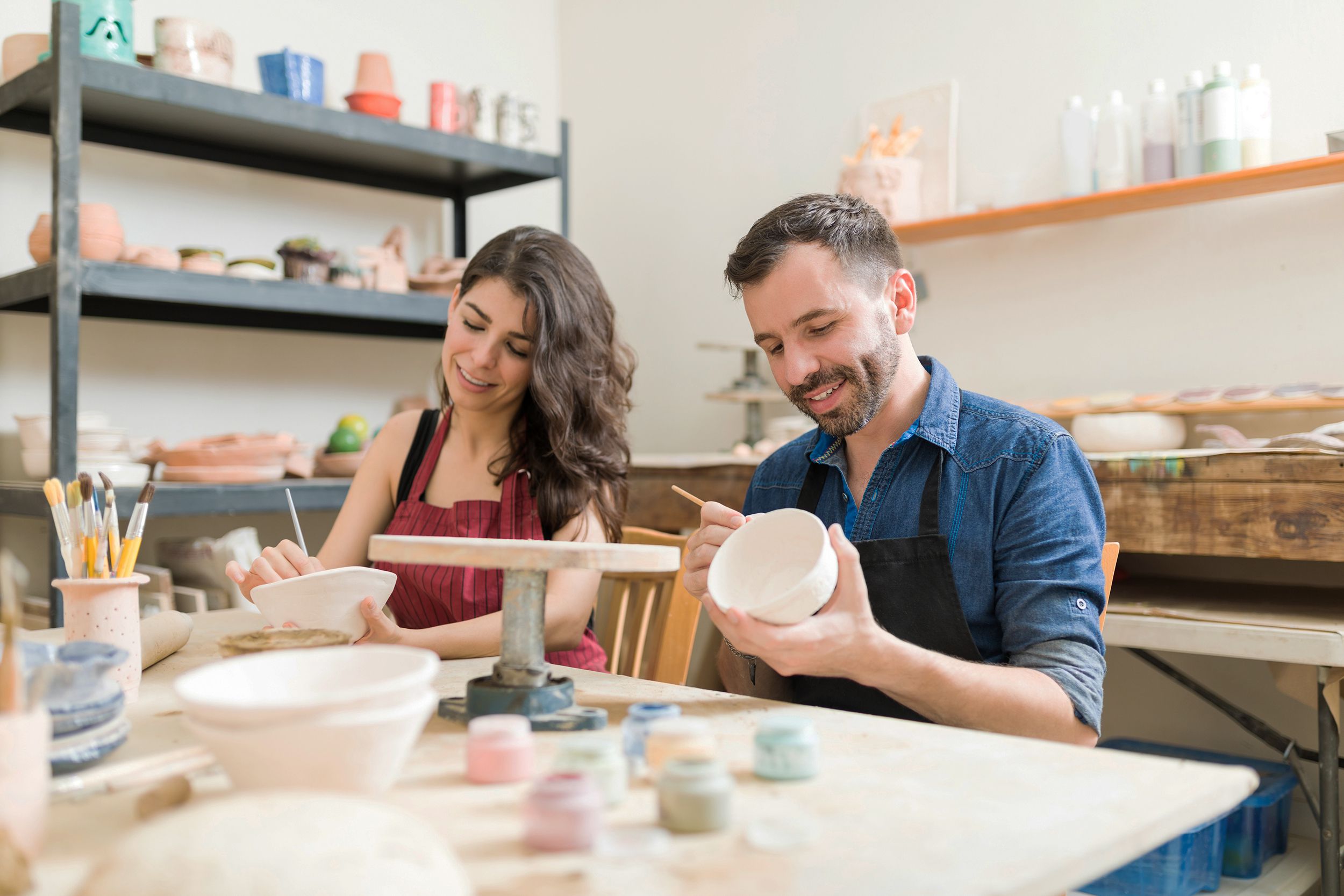 smiling couple doing creative painting on bowls in pottery workshop